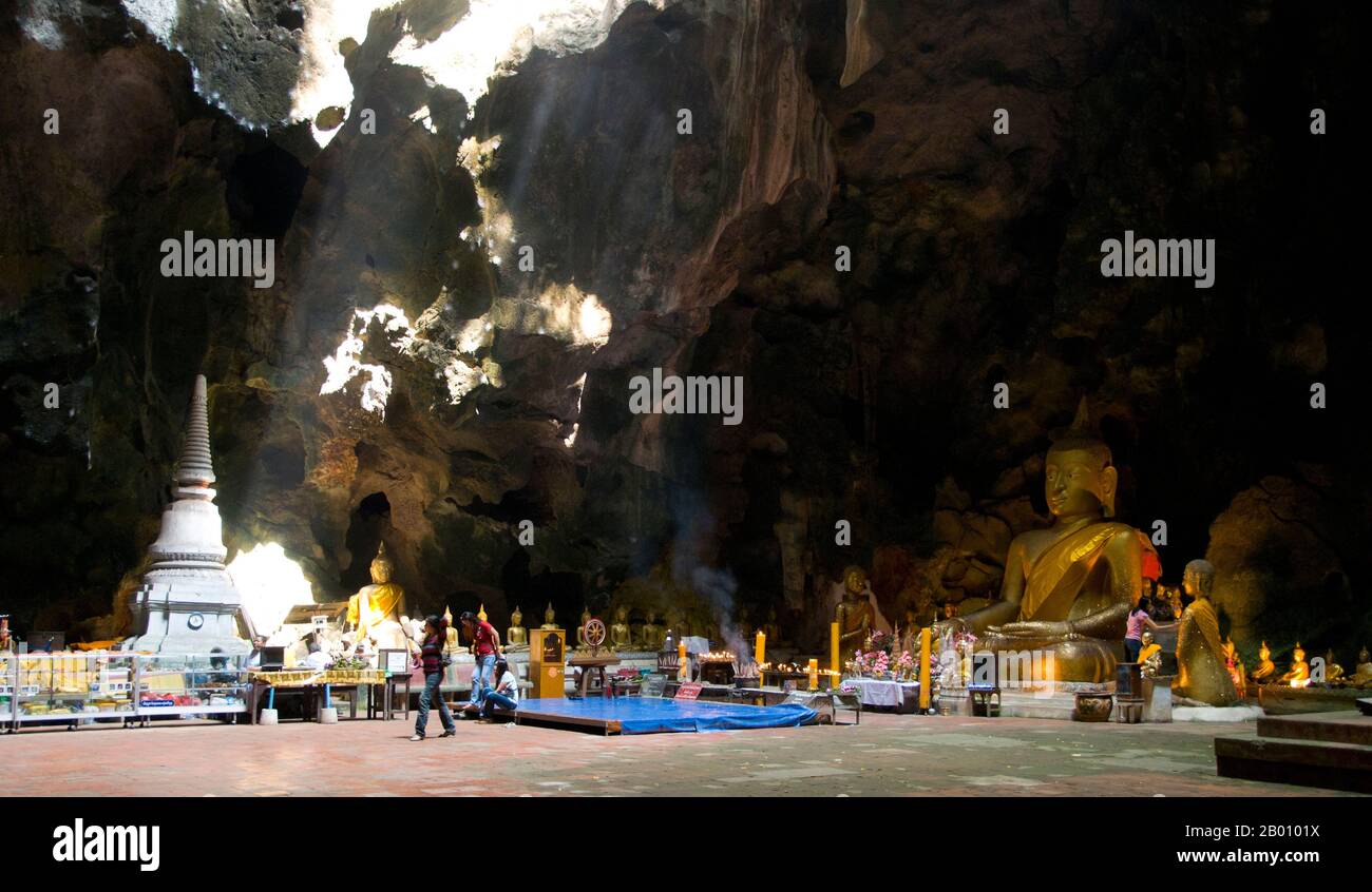 Thailand: Worshippers inside the main cavern at Tham Khao Luang, Phetchaburi.  Tham Khao Luang is a large cave consisting of three linked chambers and is distinguished by many hanging stalactites and Buddha images, including a phra non or reclining Buddha. The main bronze image was cast on the orders of King Chulalongkorn (Rama V) and dedicated to his illustrious predecessors, Kings Rama III and Rama IV. There is a natural opening in the ceiling of the second, main chamber, through which daylight streams illuminating the images within. Stock Photo