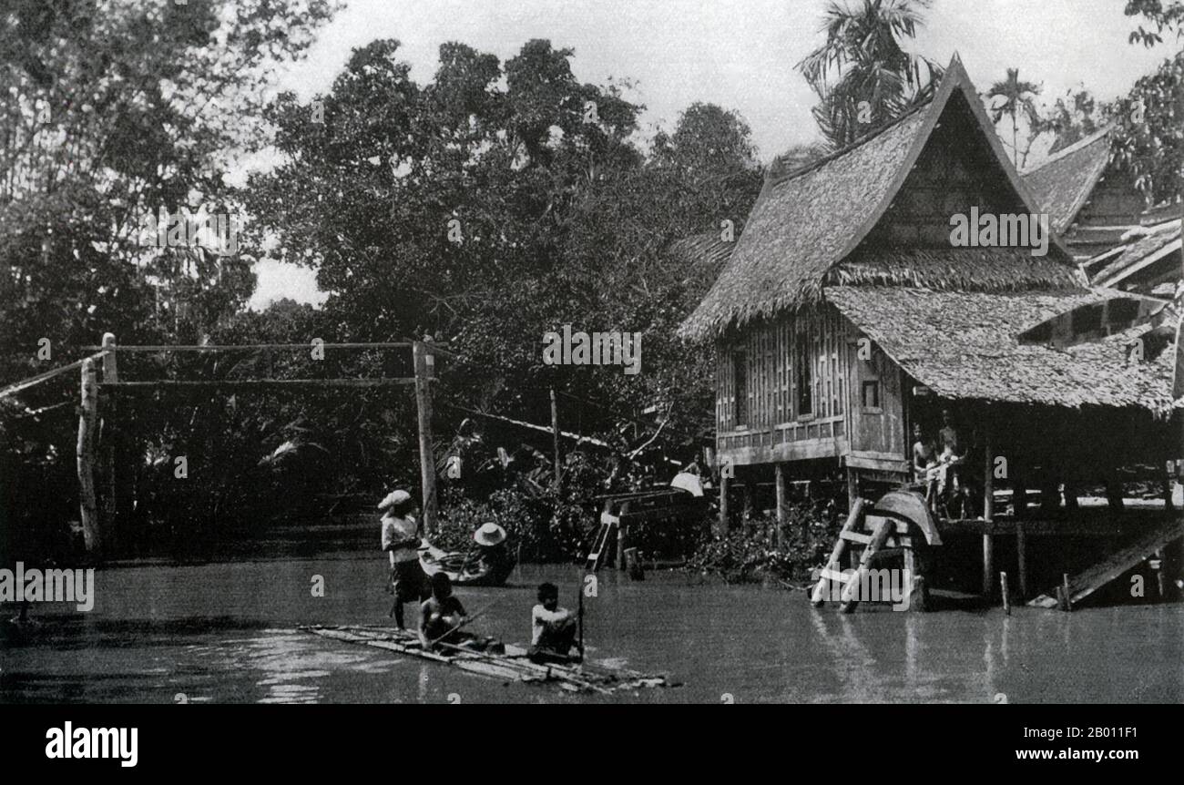 Thailand: A traditional Siamese house on stilts on a canal in Bangkok Noi, c. 1900.  At the turn of the 20th century, the vast majority of Siamese were rice farmers who lived and worked along waterways. Every household had a boat, an estimated 600,000 of which navigated the canals and rivers of Bangkok. Rowing was done from the back of the boat. Most houses were made from wood and bamboo, and were built on stilts with a ladder running to the water. Stock Photo