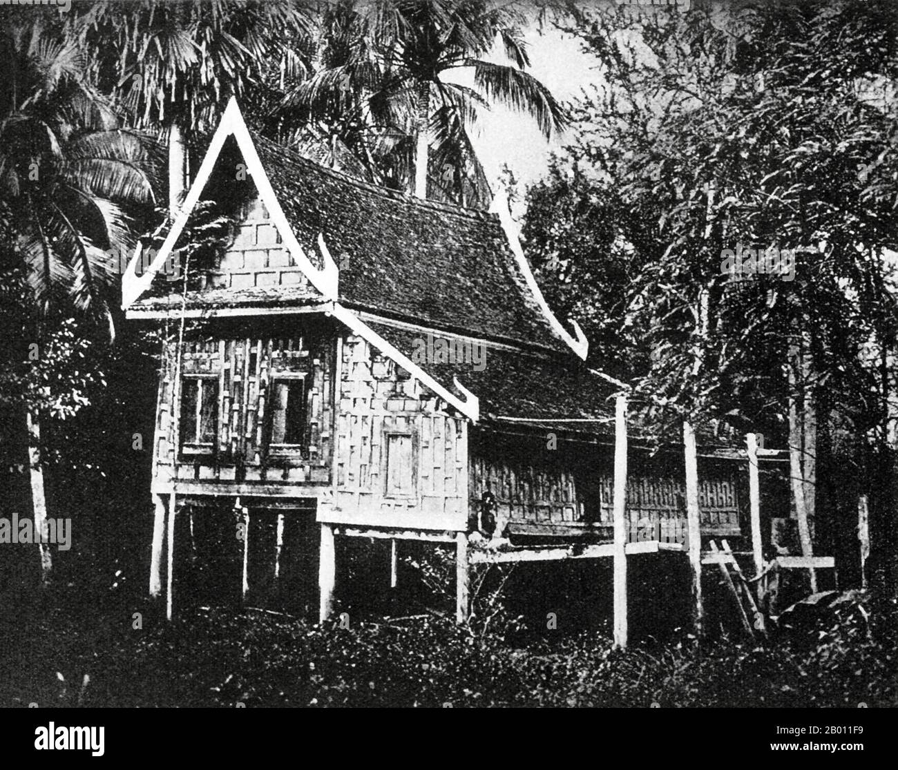 Thailand: A traditional Siamese house near Bangkok, c. 1900.  At the turn of the 20th century, the vast majority of Siamese were rice farmers who lived and worked along waterways. Every household had a boat, an estimated 600,000 of which navigated the canals and rivers of Bangkok. Rowing was done from the back of the boat. Most houses were made from wood and bamboo, and were built on stilts with a ladder running to the water. Stock Photo