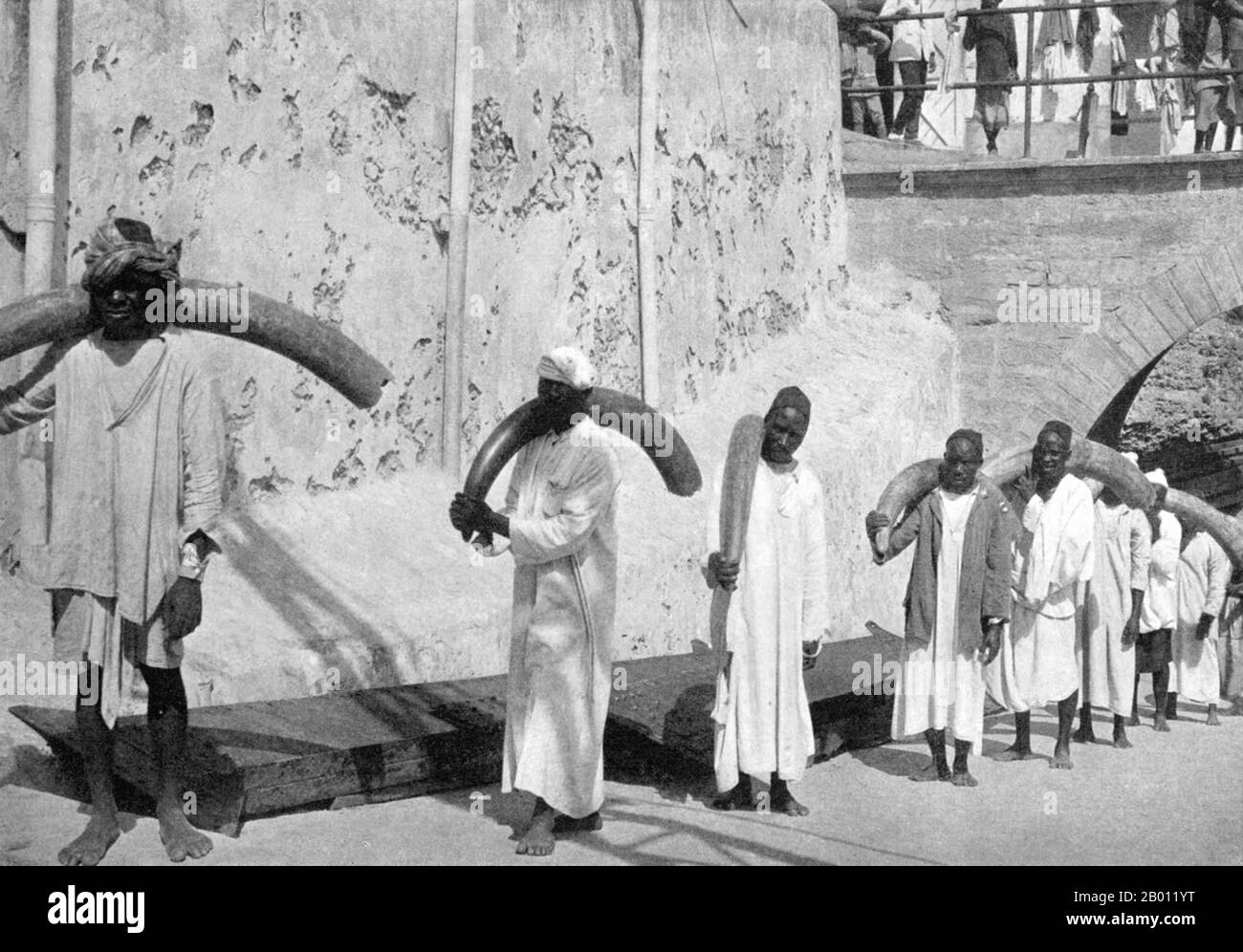 Kenya: Ivory porters carrying elephant tusks at Fort Jesus, Mombasa, c. 1922.  Elephant ivory has been exported from Africa and Asia for centuries with records going back to the 14th century BC. Throughout the colonisation of Africa ivory was removed, often using slaves to carry the tusks, to be used for piano keys, billiard balls and other expressions of exotic wealth.  Ivory hunters were responsible for wiping out elephants in North Africa perhaps about 1,000 years ago, in much of South Africa in the 19th century and most of West Africa by the end of the 20th century. Stock Photo