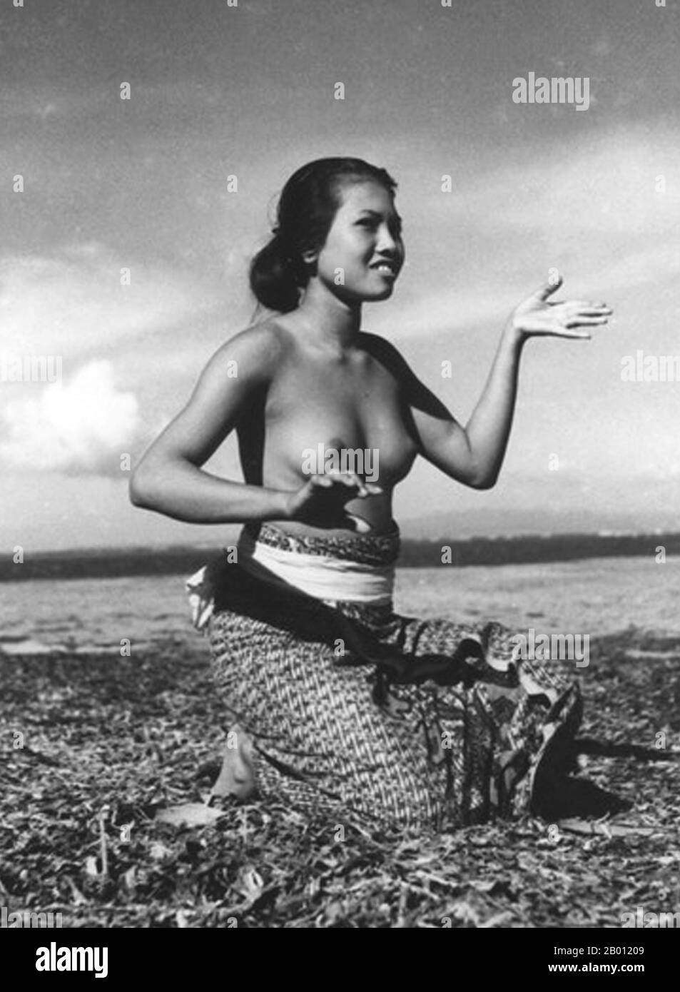 Indonesia: Young Balinese woman practicing classical dance movements by the sea shore, c. 1935.  Balinese dance is a very ancient dance tradition that is a part of the religious and artistic expression among the Balinese people, native to Bali island, Indonesia. Balinese dance is dynamic, angular and intensely expressive. The Balinese dancers express the story of dance-drama through the whole bodily gestures; fingers, hands and body gestures to head and eyes movements. Stock Photo