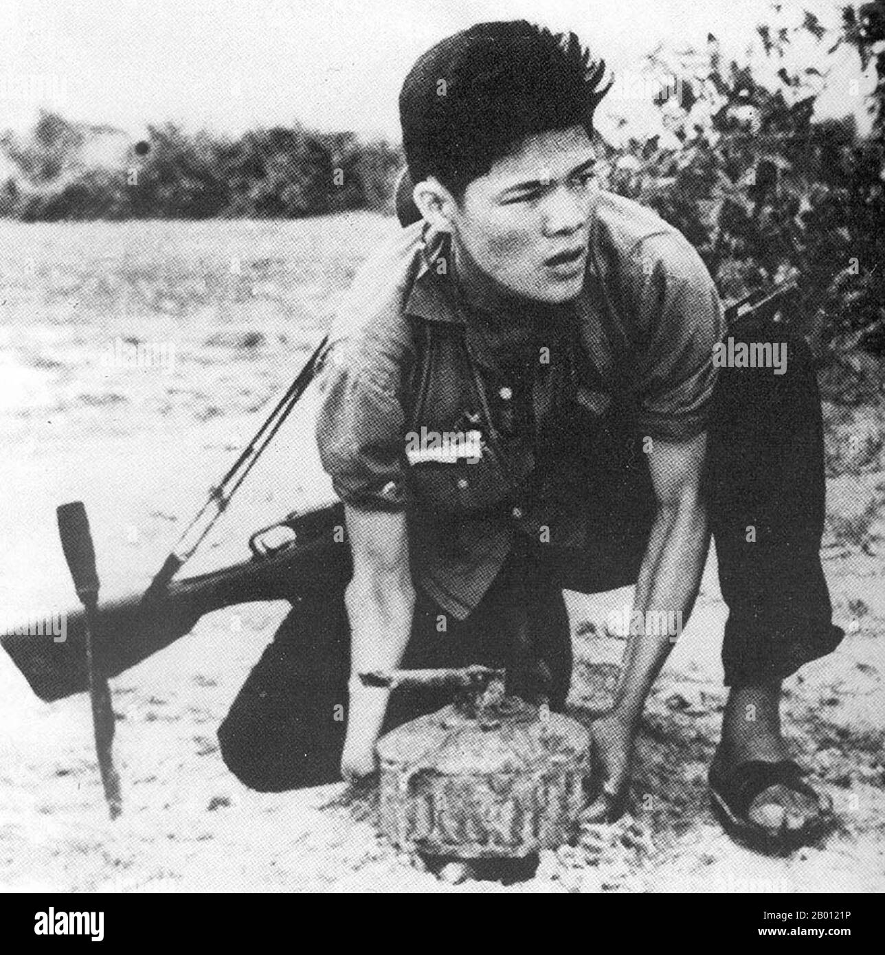 Vietnam: An NLF guerrilla posing laying a land mine for a propaganda photograph, c. 1966.  The Vietcong, or the National Front for the Liberation of South Vietnam (NLF), was a political organization and army in South Vietnam and Cambodia that fought the United States and South Vietnamese governments during the Vietnam War (1955–1975). It had both guerrilla and regular army units, as well as a network of cadres who organized peasants in the territory it controlled. Many soldiers were recruited in South Vietnam, but others were attached to the People's Army of Vietnam (PAVN). Stock Photo