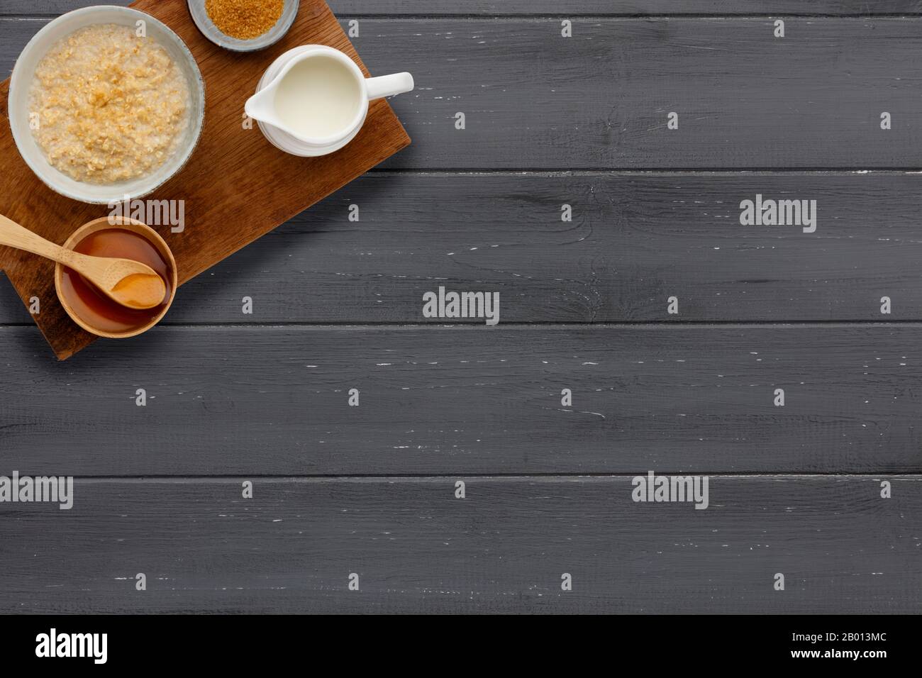 A nutritious bowl of porridge, a small bowl of brown sugar, a jug of milk and a bowl of golden syrup with a wooden spoon, on a dark wooden background, Stock Photo