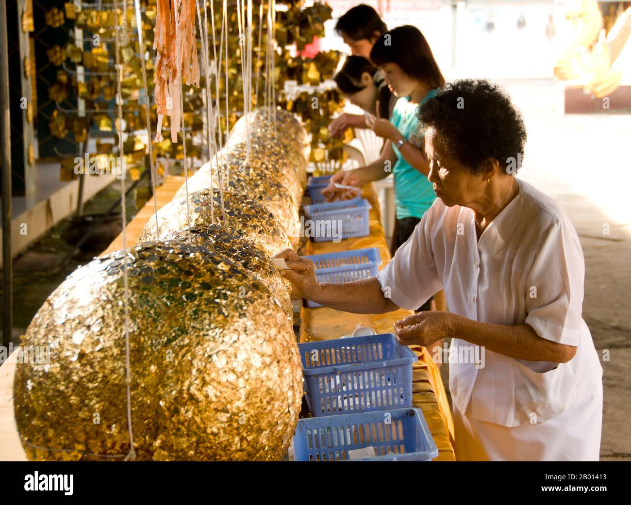 Thailand: Women plastering gold leaf on luk nimit (holy stone spheres), Wat Phrathat Doi Kham, Chiang Mai.  Luk nimit are stone spheres used for burying at the four corners and the four cardinal points of a new ubosot, a ninth is buried below the main Buddha statue.  Wat Phrathat Doi Kham or ‘Temple of the Golden Mount’, is located in Tambon Mae Hia, about 10km south of Chiang Mai Old City, in the lee of Doi Suthep. Temple records claim that the temple dates back over 1,300 years ‘to 687 CE’, during the pre-Lan Na period when the region was inhabited by the indigenous animist Lawa. Stock Photo