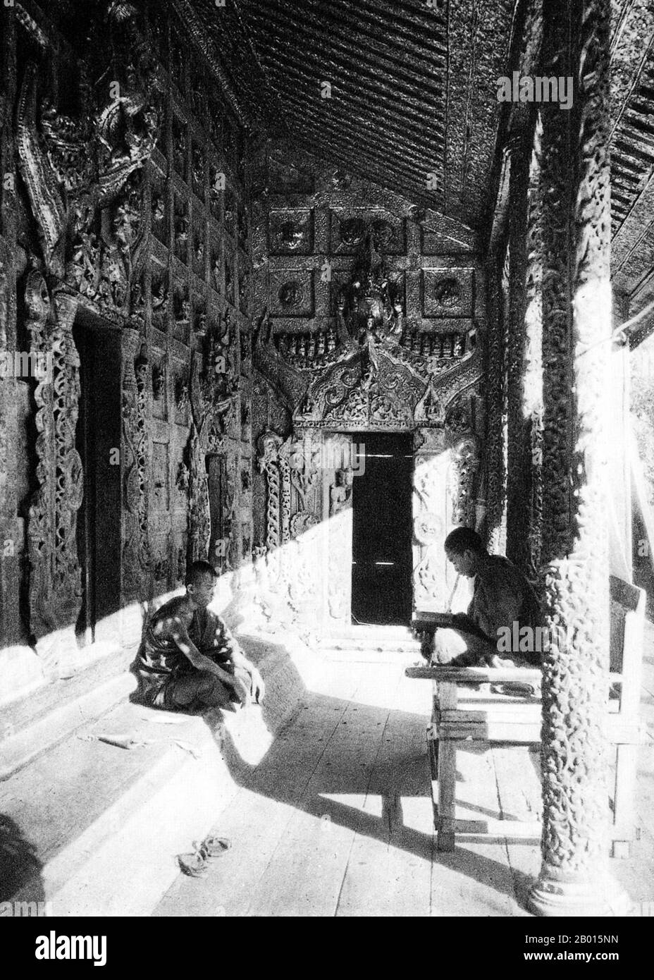 Burma/Myanmar: A Buddhist monk teaches his student in the Queen's Golden Monastery inside Mandalay Palace, c. 1920s.  The Queen's Golden Monastery was constructed on the orders of Queen Supayalat in 1885. It was barely completed when she was exiled to India with her husband Thibaw, the last king of Burma (r. 1878-1885), following the annexation of Upper Burma by the British Empire. Now destroyed, the monastery stood inside the Mandalay Palace grounds and was a magnificent wooden building lavishly decorated with ornate woodcarving and mirrored glass mosaics. Stock Photo