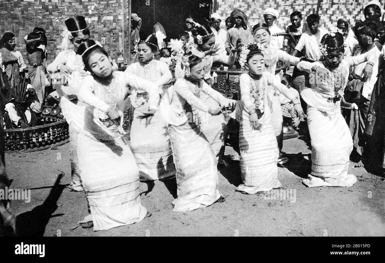 Burma/Myanmar: A young Burmese ballet troupe performs in the street accompanied by a 'saingwaing' band, c. 1920s.  A traditional Burmese orchestra, or 'saingwaing', is composed of wind instruments, Burmese trumpets ('ne'), brass gongs ('mow') and the large barrels or drum circles also known as 'saingwaing' which are lined with hanging tambourines. Troupes are still popular today at Buddhist festivals and national events. Stock Photo