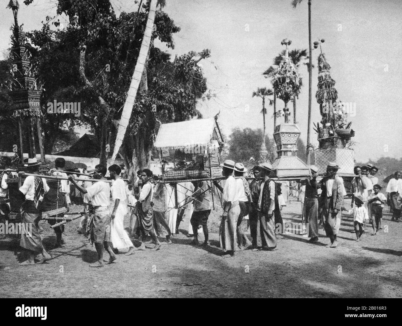 Thailand: A festival procession enters the front gates of Wat Phra That Haripunchai, Lamphun, c. 1920.  Wat Phra That Haripunchai was founded in 1044 by King Athitayarat of Haripunchai on the site of Queen Chamathewi's (Chama Thewi or Chamadevi) royal palace. Legend has it that the queen's personal quarters are enclosed in the main 46-metre high Lan Na-style chedi, covered in copper plates and topped by a gold umbrella or plee.   Lamphun was the capital of the small but culturally rich Mon Kingdom of Haripunchai from about 750 CE to the time of its conquest by King Mangrai in 1281. Stock Photo