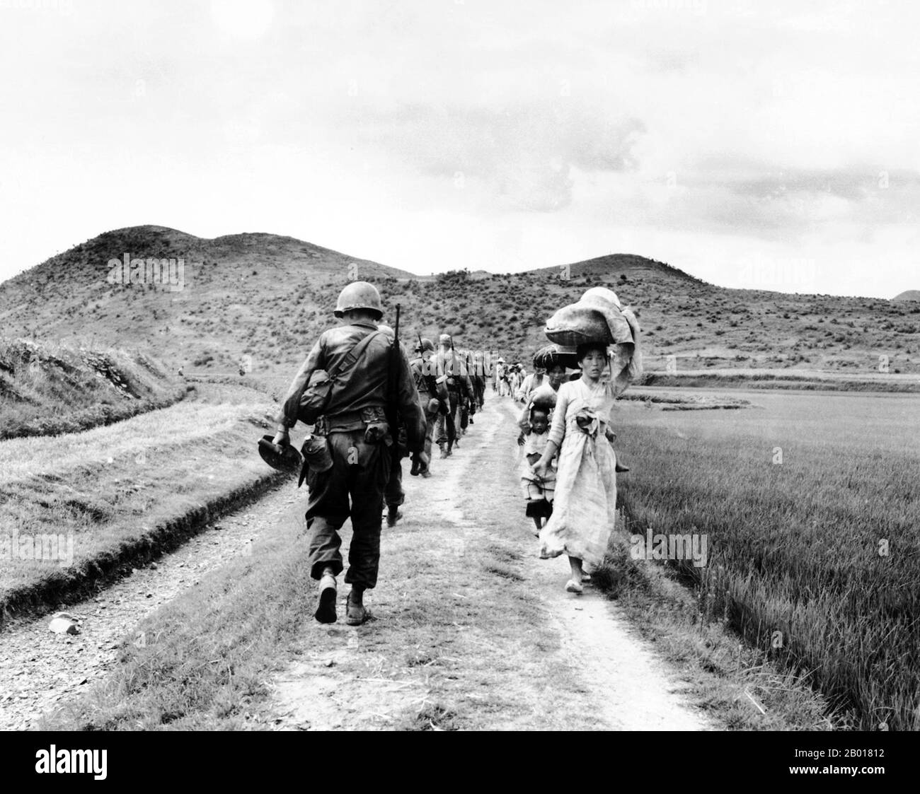 Korea: During the Korean War (25 June 1950 - armistice signed 27 July 1953), a line of US Army soldiers file past a group of Korean women and children carrying their possessions.  The Korean War was a military conflict between the Republic of Korea, supported by the United Nations, and North Korea, supported by the People's Republic of China (PRC), with military material aid from the Soviet Union. The war was a result of the physical division of Korea by an agreement of the victorious Allies at the conclusion of the Pacific War at the end of World War II. Stock Photo