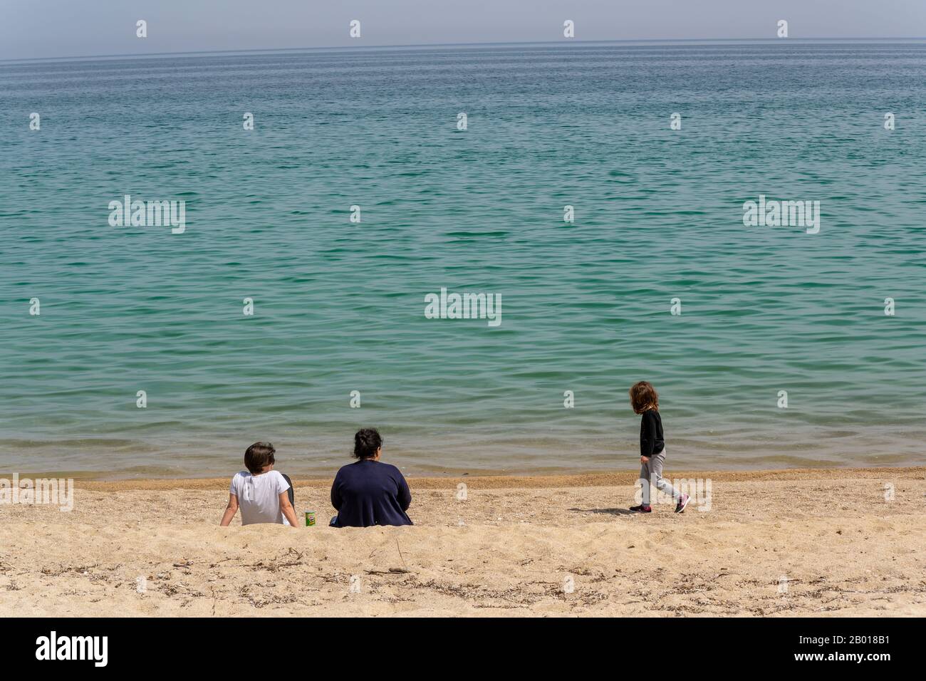 Lerissos, Greece - April 27, 2019: Three people, two children and woman at the beach of Lerissos sitting and walking at the beach with the Mediterrane Stock Photo