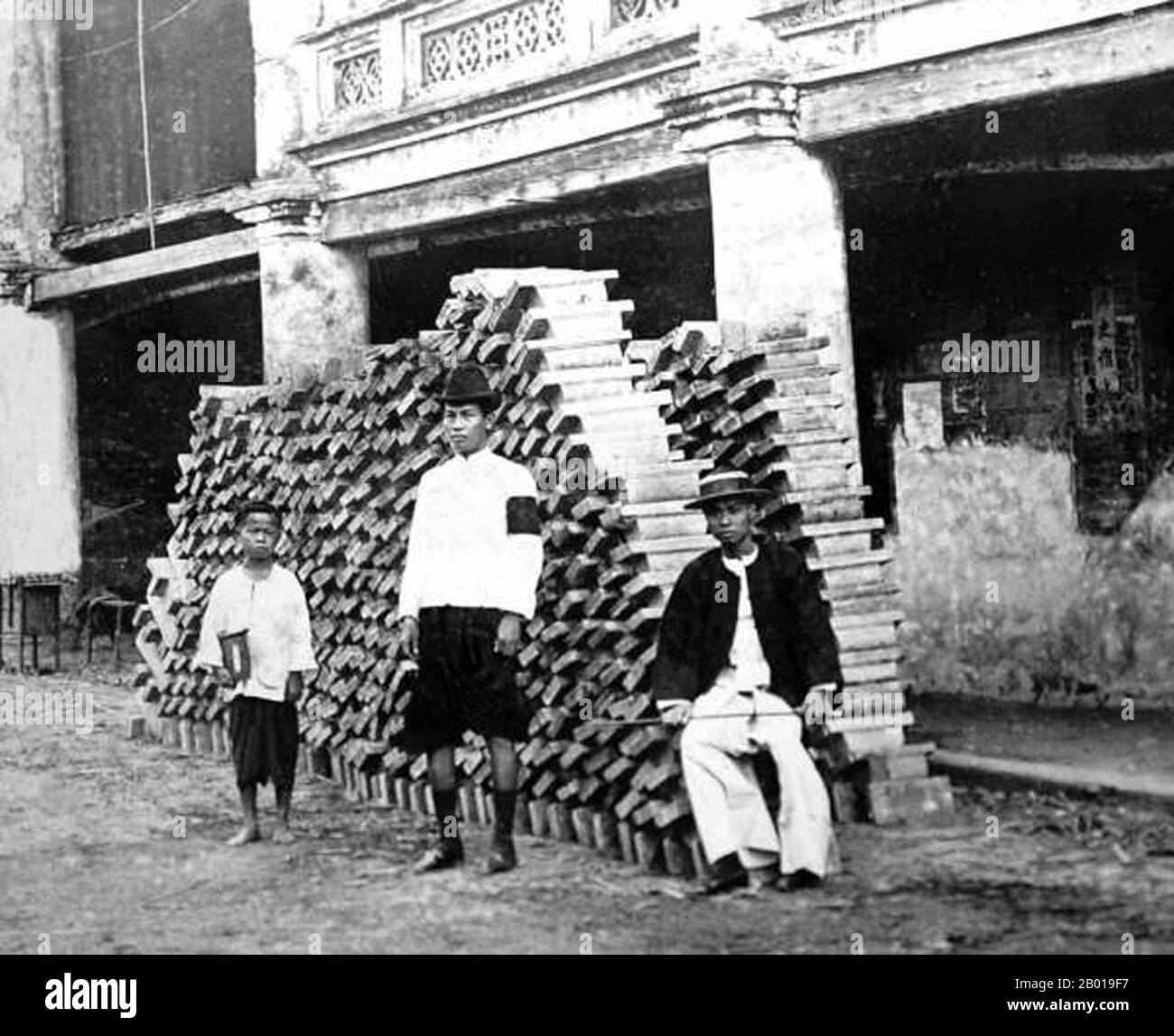 Thailand: Tin miners stand beside a pile of tin ingots stacked in front of a commercial shophouse in Phuket town, c. 1900.  Tin was discovered several centuries ago in the Kathu district of Phuket and was mined until 1992 when the last mine on Phuket closed. The tin business drew migrant workers from South China to Phuket, and many of these Overseas Chinese settled permanently in the area. Stock Photo