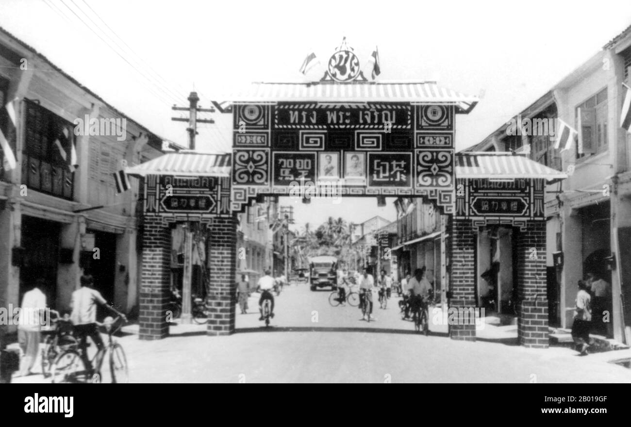 Thailand: A Chinese-style arch welcoming the King and Queen of Thailand to Phuket, 1959.  Phuket, formerly known as Talang and, in Western sources, Junk Ceylon (a corruption of the Malay Tanjung Salang, i.e. 'Cape Salang'), is one of the southern provinces (changwat) of Thailand. Neighbouring provinces are (from north clockwise) Phang Nga and Krabi, but as Phuket is an island there are no land boundaries.  Phuket, which is approximately the size of Singapore, is Thailand’s largest island. The island is connected to mainland Thailand by two bridges and is situated off the west coast. Stock Photo