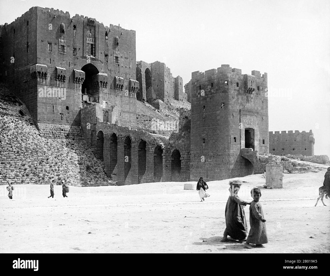 Syria: The Citadel at Aleppo (Haleb), c. 1900.  The Citadel of Aleppo is a large medieval fortified palace in the centre of the old city of Aleppo, northern Syria. One of the oldest and largest castles in the world, usage of the Citadel hill dates back to at least the middle of the 3rd millennium BCE. Subsequently occupied by many civilizations such as the Greeks, Byzantines, Ayyubids and Mamluks, the majority of the construction as it stands today is thought to originate from the Ayyubid period. Stock Photo