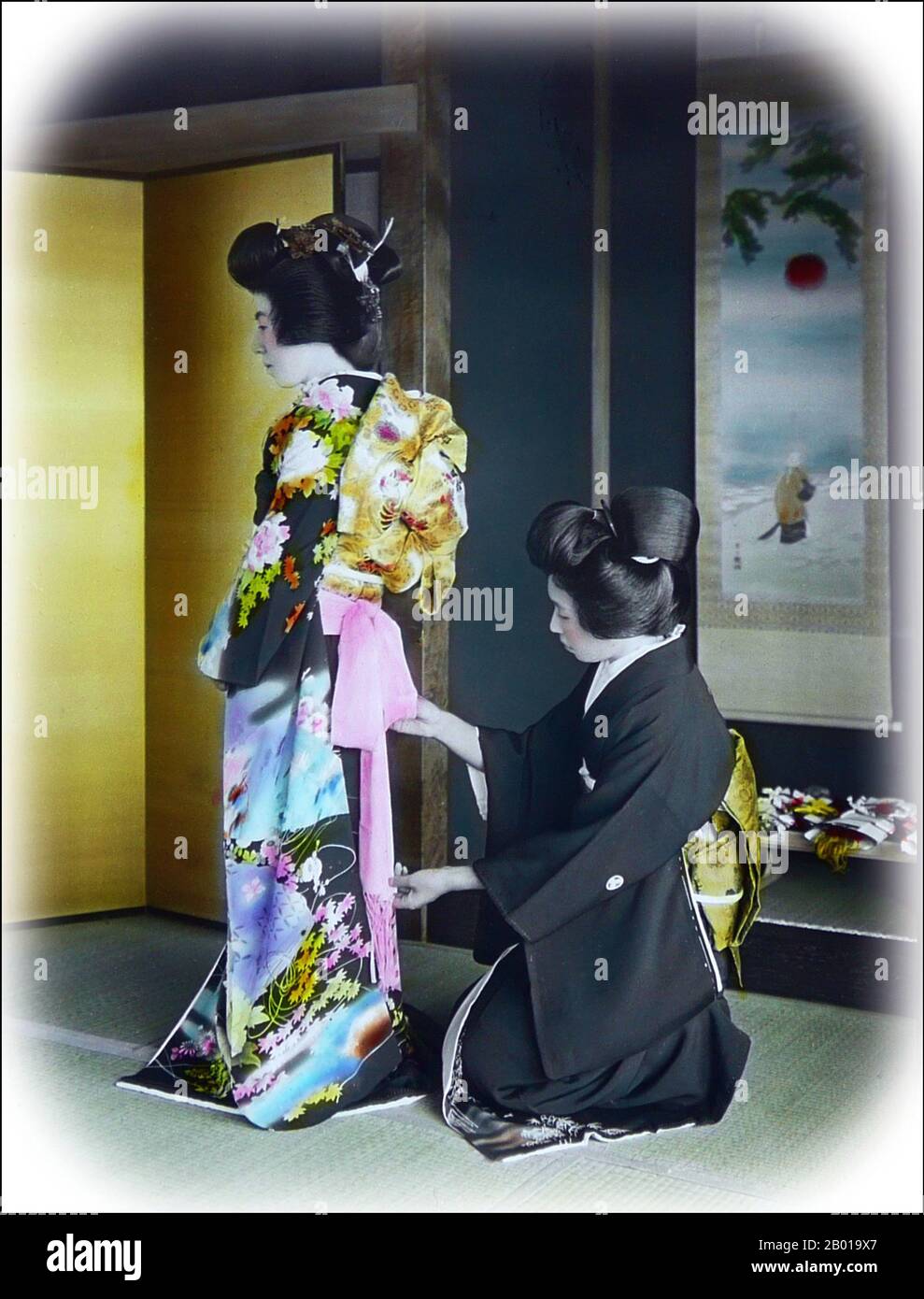 Japan: Woman arranging a kimono on another woman. Photo by T. Enami (1859-1929), c. 1895.  T. Enami (Enami Nobukuni) was the trade name of a celebrated Meiji period photographer. The T. of his trade name is thought to have stood for Toshi, though he never spelled it out on any personal or business document.  Born in Edo (now Tokyo) during the Bakumatsu era, Enami was first a student of, and then an assistant to the well known photographer and collotypist, Ogawa Kazumasa. Enami relocated to Yokohama, and opened a studio on Benten-dōri (Benten Street) in 1892. Stock Photo
