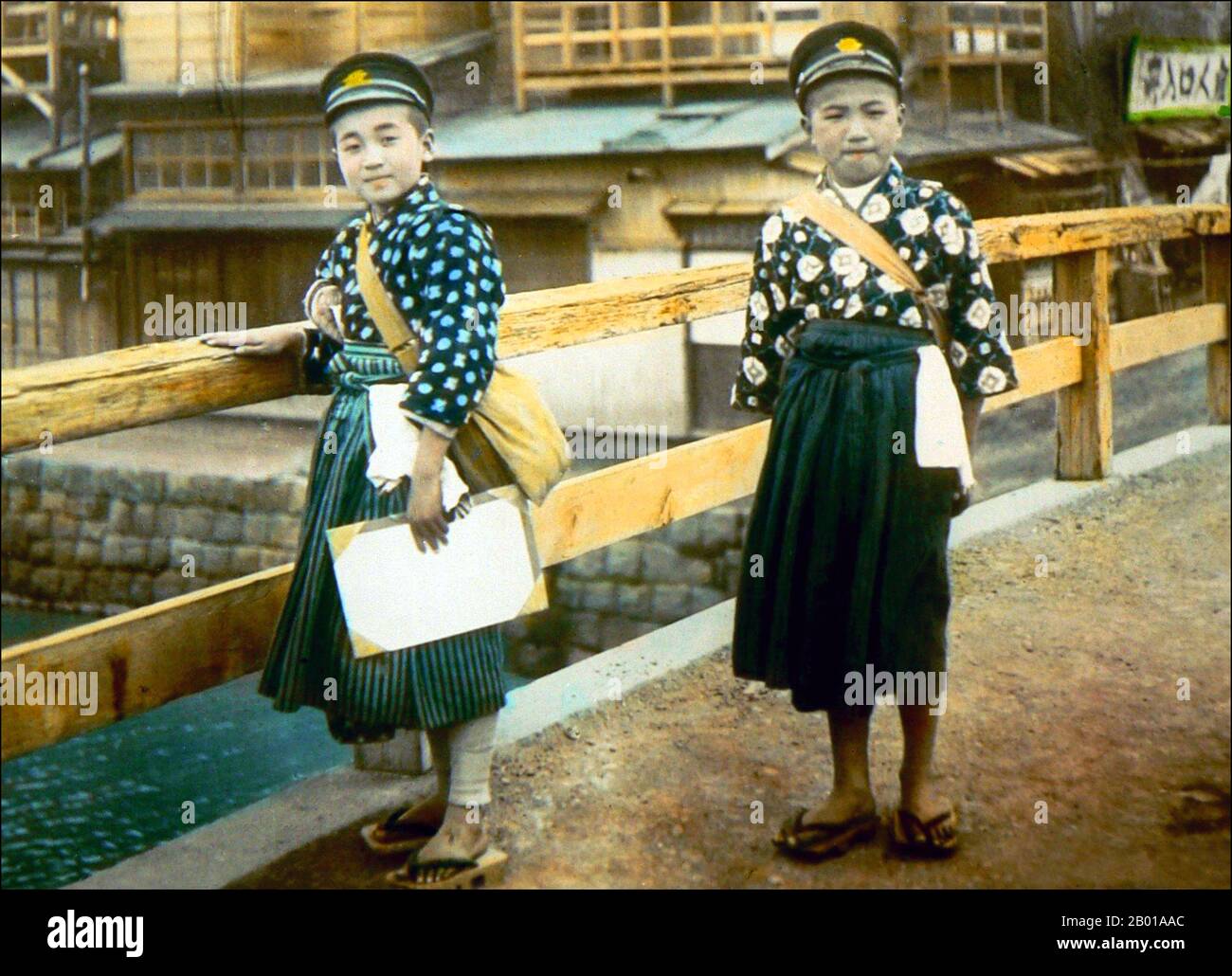 Japan: Two young schoolboys on their way to school. Photo by T. Enami (1859-1929), c. 1910.  T. Enami (Enami Nobukuni) was the trade name of a celebrated Meiji period photographer. The T. of his trade name is thought to have stood for Toshi, though he never spelled it out on any personal or business document.  Born in Edo (now Tokyo) during the Bakumatsu era, Enami was first a student of, and then an assistant to the well known photographer and collotypist, Ogawa Kazumasa. Enami relocated to Yokohama, and opened a studio on Benten-dōri (Benten Street) in 1892. Stock Photo