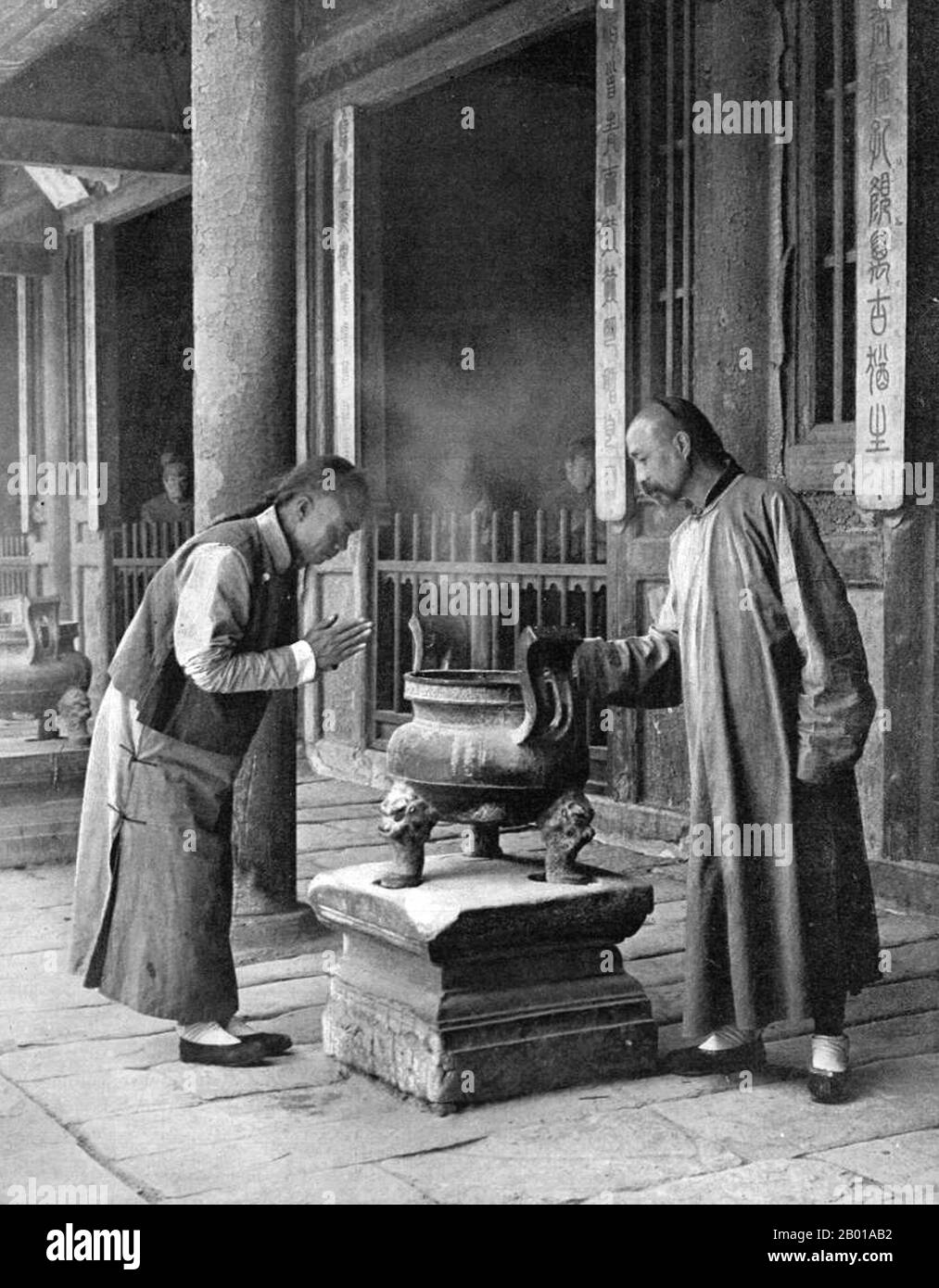 China: Two men by an incense burner in a temple in Beijing. Photo by Herbert Ponting (21 March 1870 - 7 February 1935), c. 1907.  Of this scene Ponting notes: 'The Chinese are not a religious people. Confucianism, which dominates the Chinaman's life, being, properly speaking, a code of ethics. Yet many religions exist in China, among which are Buddhism, Mahommedanism (Islam) and Taoism.'  Herbert George Ponting was a photographer from England. He was best known for being the photographer and cinematographer for Robert Falcon Scott's Terra Nova Expedition to the Ross Sea and South Pole. Stock Photo