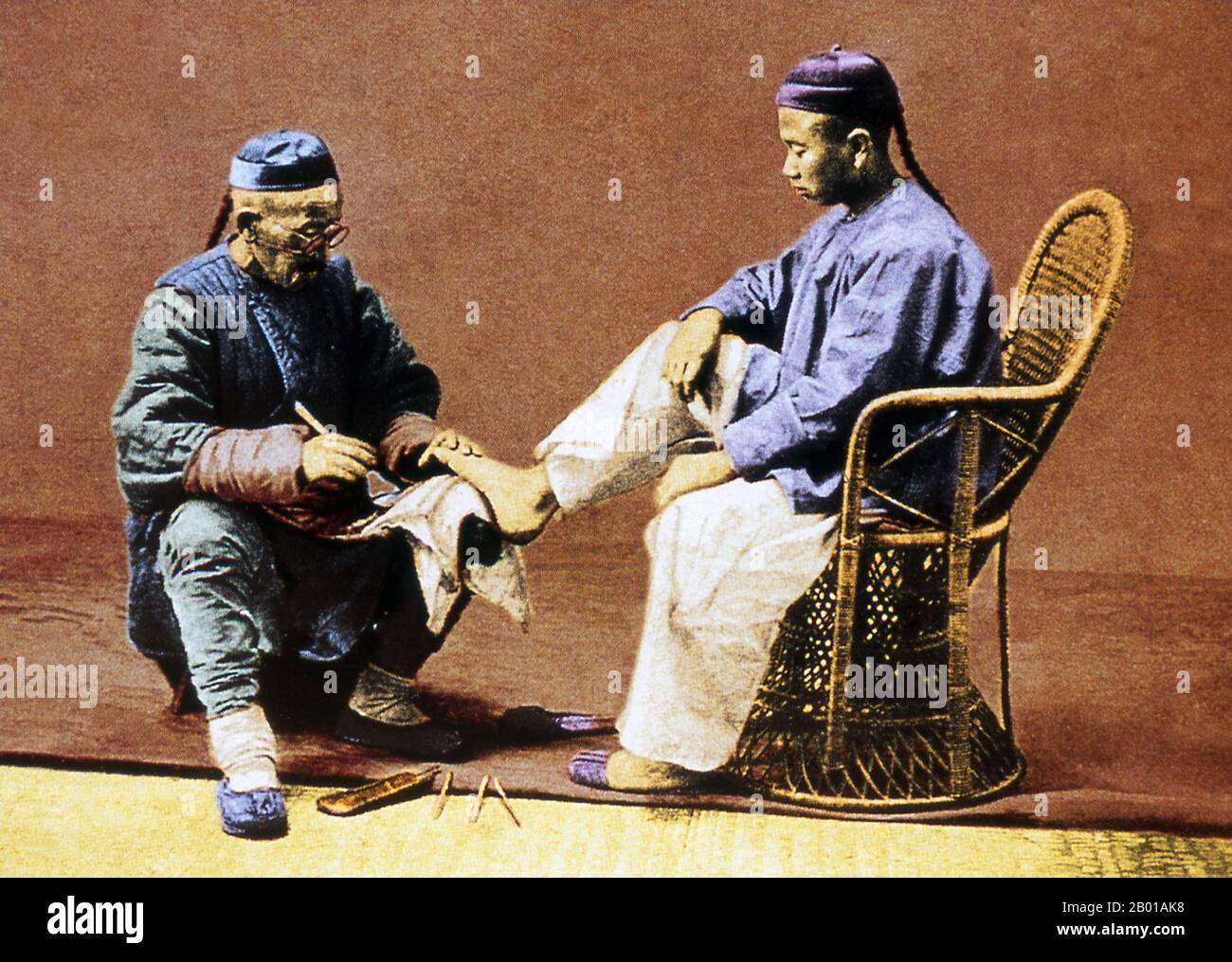China: Man receiving a pedicure, Beijing, c. 1890.  In old China pedicures - and pedicurists - were often mobile. The Chinese term for pedicure is 'xiu jiao di'. A pedicure is a way to improve the appearance of the feet and their nails. It provides a similar service to a manicure. The word pedicure refers to superficial cosmetic treatment of the feet and toenails and comes from the Latin words pedis, which means 'of the foot', and cura, which means 'care'. Stock Photo