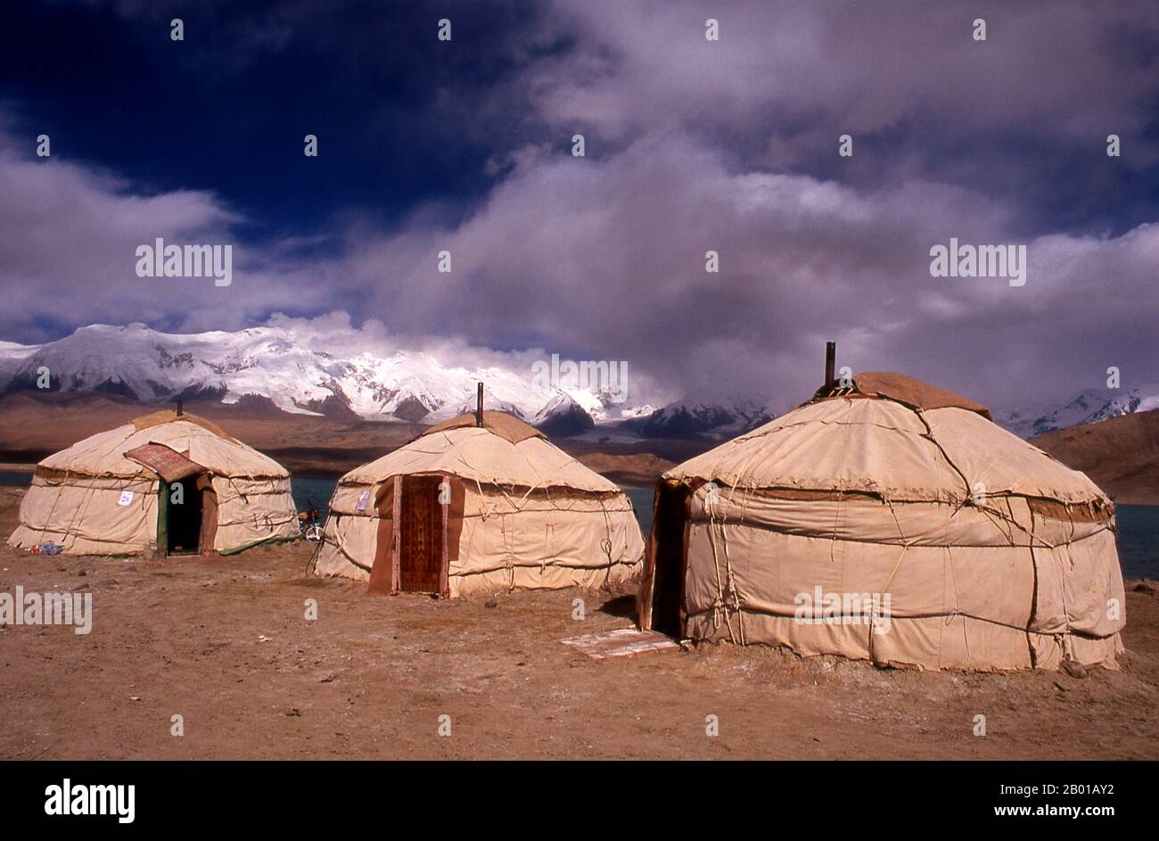 China: Kirghiz yurts at Lake Karakul on the Karakoram Highway, Xinjiang.  Two small settlements of Kirghiz (Kyrgyz or Kirgiz) nomads lie by the side of Lake Karakul high up in the Pamir Mountains. Visitors can stay overnight in one of their mobile homes or yurts – Kirghiz men will approach travellers as they arrive at the lake and offer to arrange this accommodation. The Kyrgyz form one of the 56 ethnic groups officially recognized by the People's Republic of China. There are more than 145,000 Kyrgyz in China.  The Zhongba Gonglu or Karakoram Highway is an engineering marvel. Stock Photo