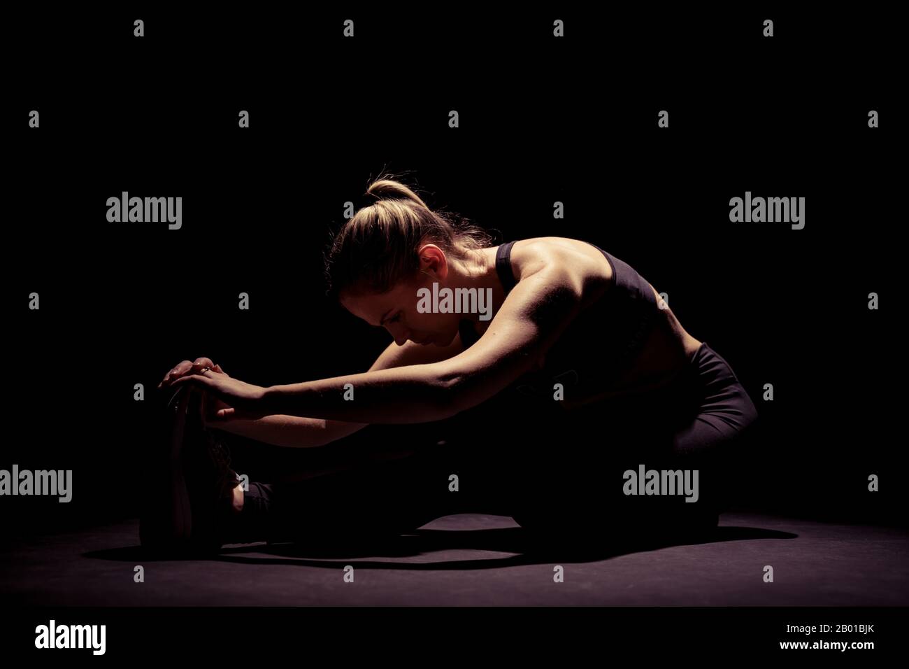 Fit female model in sport clothing doing exercises in the studio with black background with copy space. Stock Photo