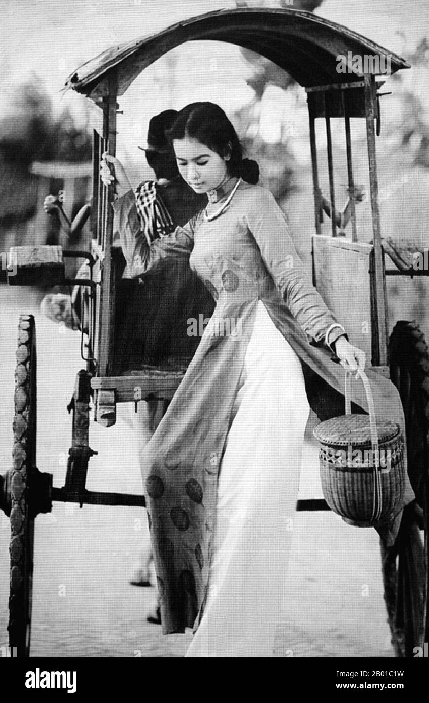 Vietnam: Young woman in an ao dai dress descending from a covered pony cart, Saigon, 1950s.  The ao dai (Vietnamese: áo dài) is a Vietnamese national costume, now most commonly for women. In its current form, it is a tight-fitting silk tunic worn over pantaloons. The word is pronounced ow-zye in the north and ow-yai in the south, and translates as 'long dress'.  The name áo dài was originally applied to the dress worn at the court of the Nguyễn Lords at Huế in the 18th century. This outfit evolved into the áo ngũ thân, a five-paneled aristocratic gown worn in the 19th and early 20th centuries. Stock Photo
