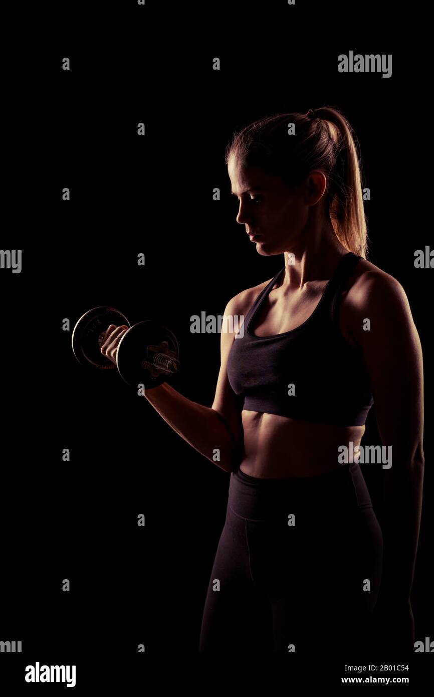 Fit female model in sport clothing doing exercises in the studio with black background with copy space. Stock Photo