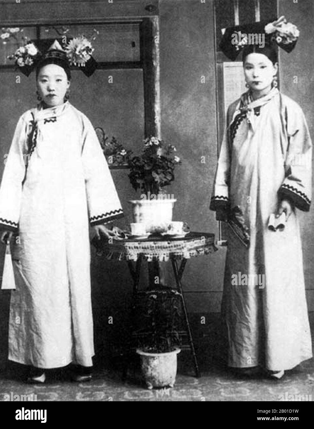 China: Manchu ladies at the Qing Imperial Court in Beijing, c. 1890.  Manchu women of the Forbidden City or Gugong in Beijing pose for a photograph during the Manchu Qing Dynasty (1644-1911). They wear elaborate and expensive dresses. Their faces are whitened with powder, and their lipstick is applied in a narrow band across the centre of their lips following the fashion of the time. Stock Photo