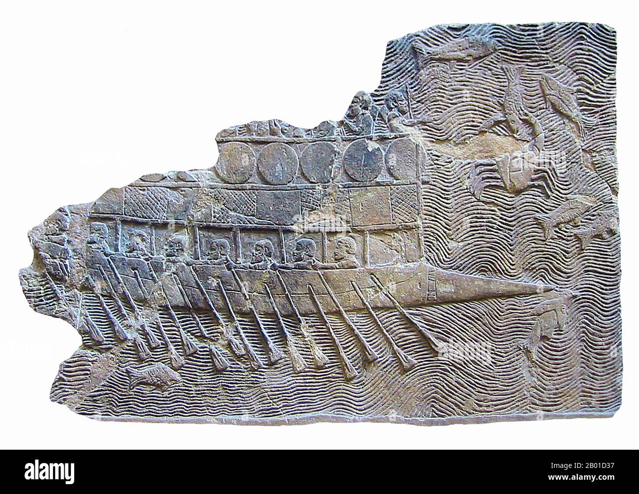 Iraq: Fragment of a bas-relief of an Assyrian warship from the Palace at Nineveh, c. 700 BCE. Photo by World Imaging (CC BY-SA 3.0 License).  This Assyrian ship was probably built and possibly manned by Phoenicians employed by Sennacherib, the son of Sargon II of Akkad, whom he succeeded on the throne of Assyria (705–681 BCE).  It is a bireme, with two rows of oars. Shields are fastened around the superstructure, as on the fortifications of some city walls. The pointed bow is a ram, for piercing enemy shipping. Stock Photo