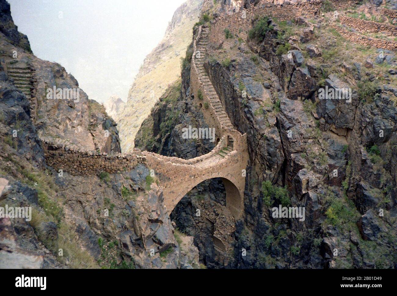 Yemen: Footbridge across a 300 metre (985 ft) chasm at Shahara, north of Sana'a. Photo by Bernard Gagnon (CC BY-SA 3.0 License), 1986.  The celebrated Shahara Bridge in Yemen was built across a 300-metre deep gorge in 1620, ostensibly to repel Turkish invasions. Shaharah is a fortified village high in the Yemeni Sarawat Mountains about six hours drive north of Sana'a.  Fortified mountain villages are common in Yemen, but Shaharah is the most inaccessible. Incredibly inaccessible, Shaharah has been a thorn in the side of any invading army and a bolthole for retreating imams for centuries. Stock Photo