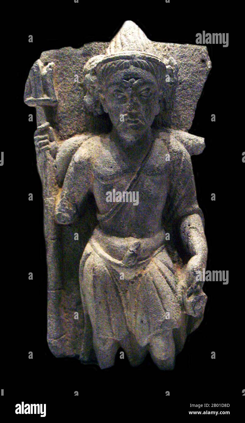 Pakistan/Afghanistan: Shiva with trident, Gandhara, 2nd century CE. Photo by PHGCOM (CC BY-SA 3.0 License).  Gandhāra is noted for the distinctive Gandhāra style of Buddhist art, which developed out of a merger of Greek, Syrian, Persian, and Indian artistic influence. This development began during the Parthian Period (50 BCE - 75 CE). Gandhāran style flourished and achieved its peak during the Kushan period, from the 1st to the 5th century. It declined and suffered destruction after invasion of the White Huns in the 5th century.  Stucco as well as stone was widely used by sculptors in Gandhara Stock Photo