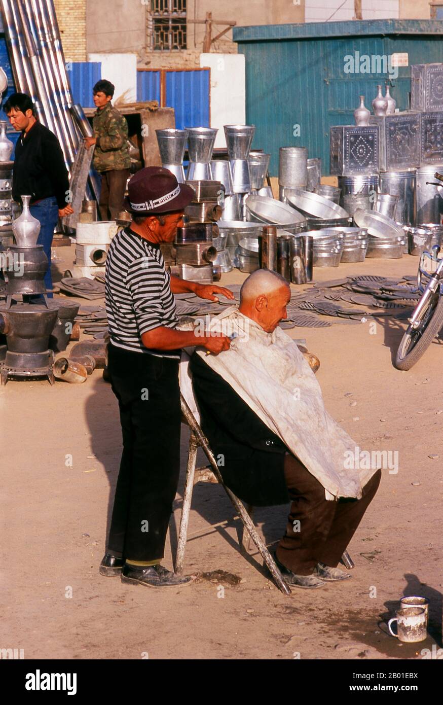 China: Outdoor barber, Old Kuqa, Xinjiang Province.  The ancient oasis town of Kuqa (Kuche), though now overshadowed by Korla to the east and Aksu to the west, was once a key stop on the Northern Silk Road. It first came under Han Chinese control when it was conquered, in 91 CE, by the indomitable General Ban Chao.  By the 4th century it had emerged as an important centre of Tocharian civilisation sitting astride not just the Northern Silk Road, but also lesser routes to Dzungaria in the north and Khotan in the south. The celebrated Buddhist monk Kumarajiva was born here. Stock Photo
