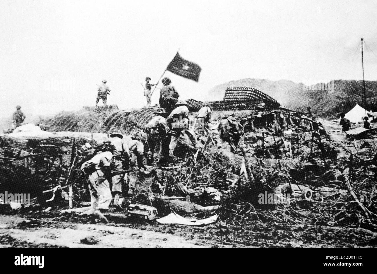 Vietnam: Victorious Viet Minh troops wave a Vietnamese flag over captured French command post at Dien Bien Phu, May 7, 1954.  The important Battle of Dien Bien Phu was fought between the Việt Minh (led by General Vo Nguyen Giap), and the French Union (led by General Henri Navarre, successor to General Raoul Salan). The siege of the French garrison lasted fifty-seven days, from 5:30 PM on March 13 to 5:30 PM on May 7, 1954.  The southern outpost or fire base of the camp, Isabelle, did not follow the cease-fire order and fought until the next day at 01:00 AM. Stock Photo