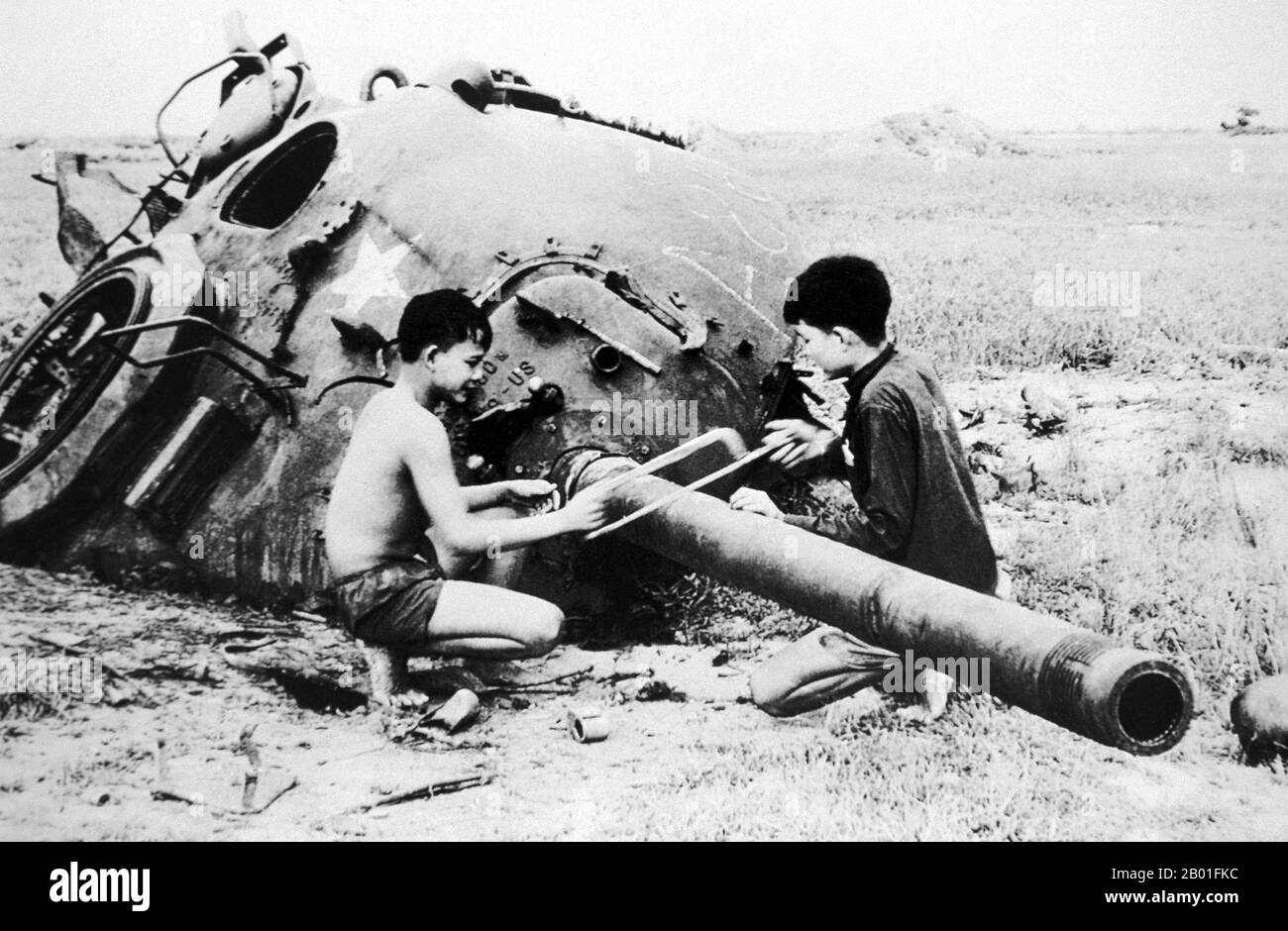 Vietnam: NLF children sawing barrel off destroyed US tank, Cu Chi, 1968.  The Second Indochina War, known in America as the Vietnam War, was a Cold War era military conflict that occurred in Vietnam, Laos, and Cambodia from 1 November 1955 to the fall of Saigon on 30 April 1975. This war followed the First Indochina War and was fought between North Vietnam, supported by its communist allies, and the government of South Vietnam, supported by the U.S. and other anti-communist nations. The U.S. government viewed involvement in the war as a way to prevent a communist takeover of South Vietnam. Stock Photo