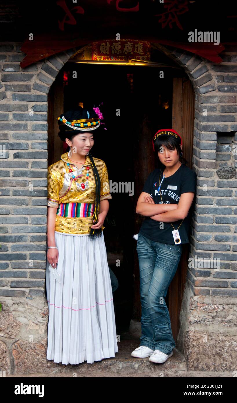 China: Mosuo girl and friend outside a restaurant in Lijiang Old Town, Yunnan Province.  The Mosuo (also Moso or Musuo), but known often to themselves as the Na, are a small ethnic group living in Yunnan and Sichuan Provinces, close to the border with Tibet. With a population of approximately 40,000, most of them live in the Yongning region and around Lugu Lake, high in the Tibetan Himalayas.  Although the Mosuo are culturally distinct from the Nakhi, the Chinese government places them as members of the Nakhi (aka Naxi) minority.  The Old Town of Lijiang dates back more than 800 years. Stock Photo