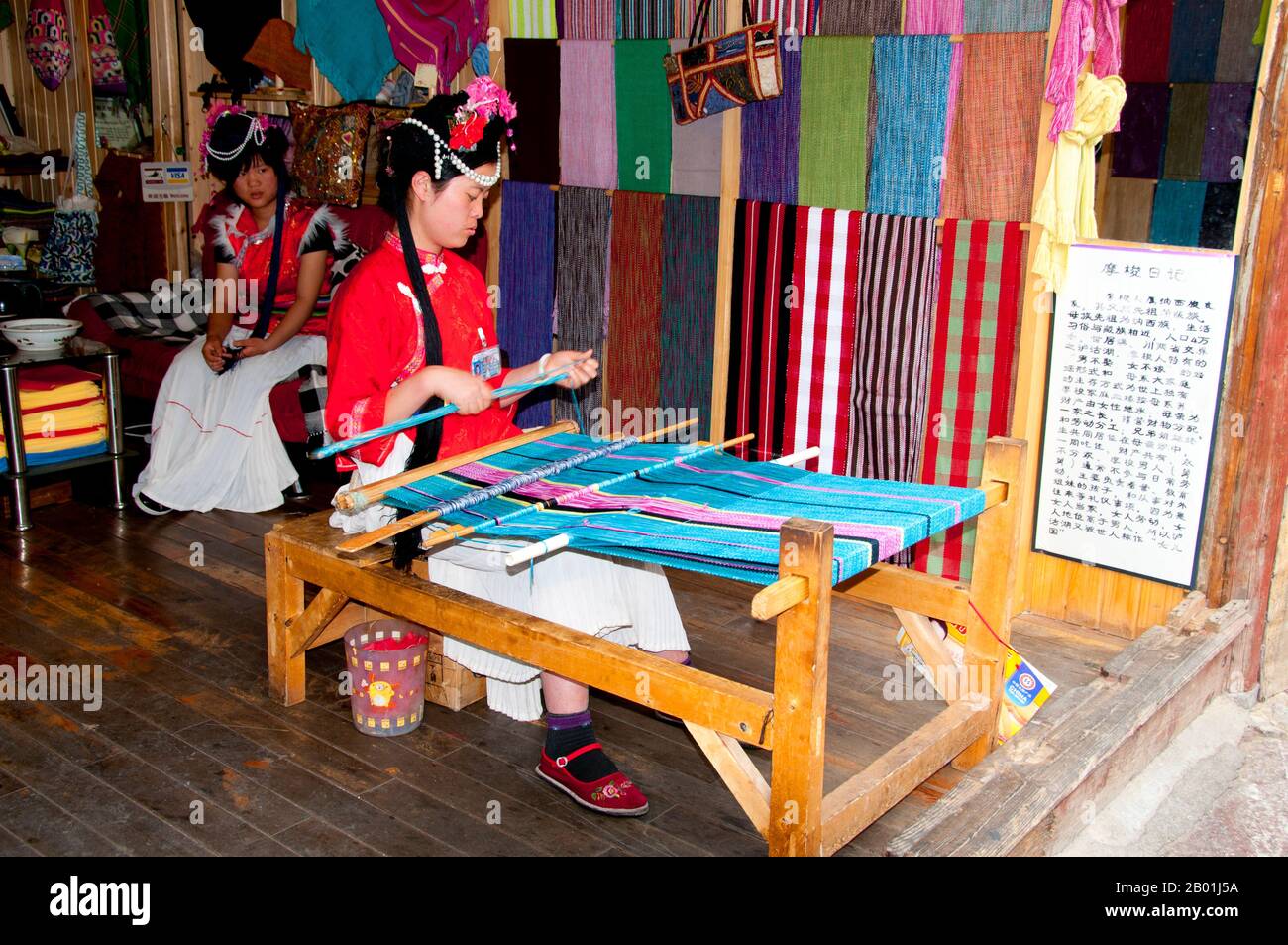 China: Mosuo woman weaving in Lijiang Old Town, Yunnan Province.  The Mosuo (also Moso or Musuo), but known often to themselves as the Na, are a small ethnic group living in Yunnan and Sichuan Provinces, close to the border with Tibet. With a population of approximately 40,000, most of them live in the Yongning region and around Lugu Lake, high in the Tibetan Himalayas.  Although the Mosuo are culturally distinct from the Nakhi, the Chinese government places them as members of the Nakhi (aka Naxi) minority.  The Old Town of Lijiang dates back more than 800 years and was once an important town. Stock Photo