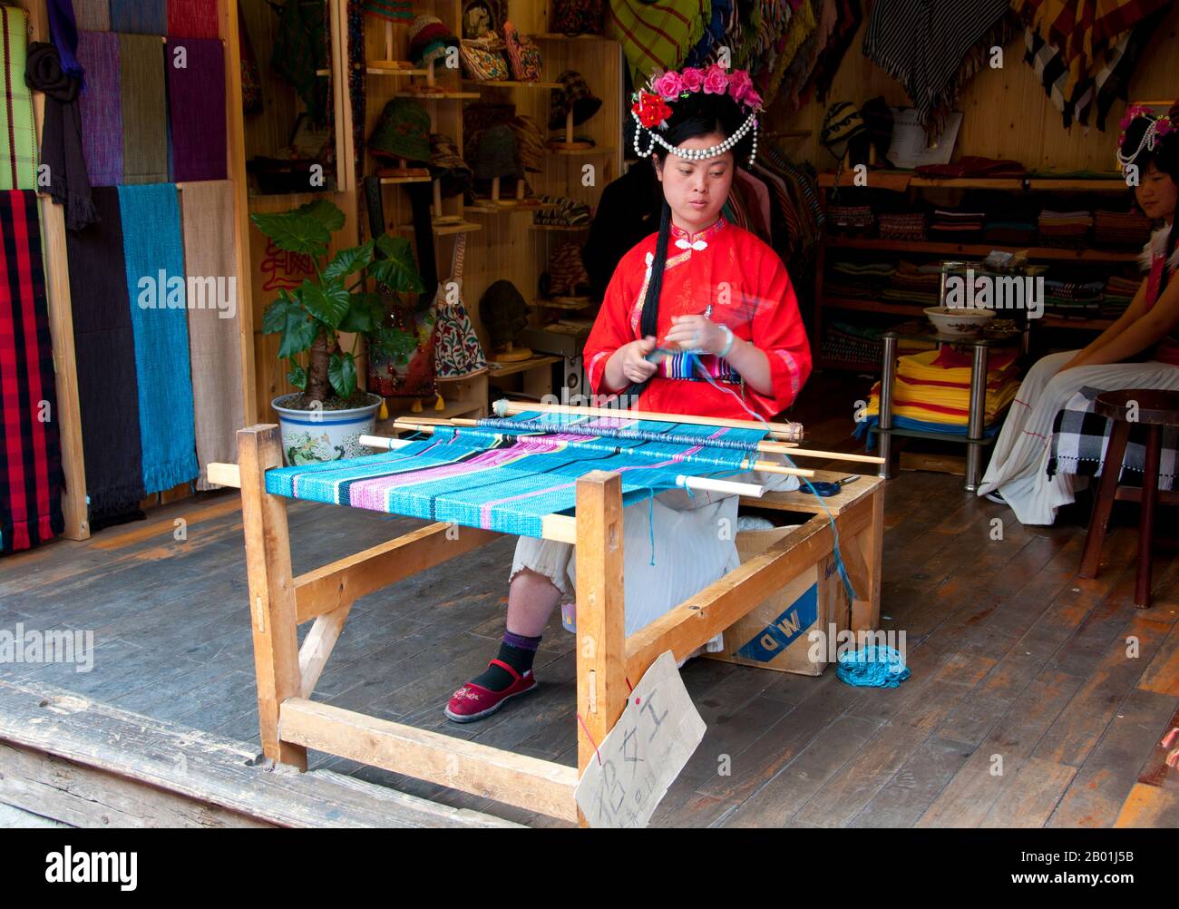 China: Mosuo woman weaving in Lijiang Old Town, Yunnan Province.  The Mosuo (also Moso or Musuo), but known often to themselves as the Na, are a small ethnic group living in Yunnan and Sichuan Provinces, close to the border with Tibet. With a population of approximately 40,000, most of them live in the Yongning region and around Lugu Lake, high in the Tibetan Himalayas.  Although the Mosuo are culturally distinct from the Nakhi, the Chinese government places them as members of the Nakhi (aka Naxi) minority.  The Old Town of Lijiang dates back more than 800 years and was once an important town. Stock Photo