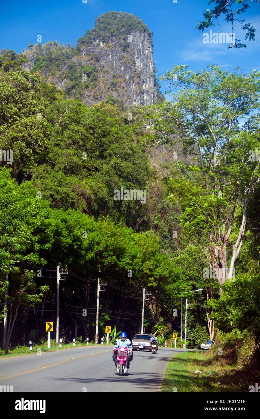 Thailand: Motorcyclist and limestone peak, Krabi Province.  Krabi Province is made up of more than 5,000 sq km of jungle-covered hills and sharp, jagged karst outcrops, as well as more than 100 km of pristine coastline and around 200 islands in the neighbouring Andaman Sea.  About 40 per cent of the provincial population is Muslim, the remainder being predominantly Buddhist. This is a clear indication that Krabi sits astride the invisible dividing line between Buddhist Thailand and the four southern provinces - Satun, Narathiwat, Yala and Pattani - which are predominantly Muslim. Stock Photo