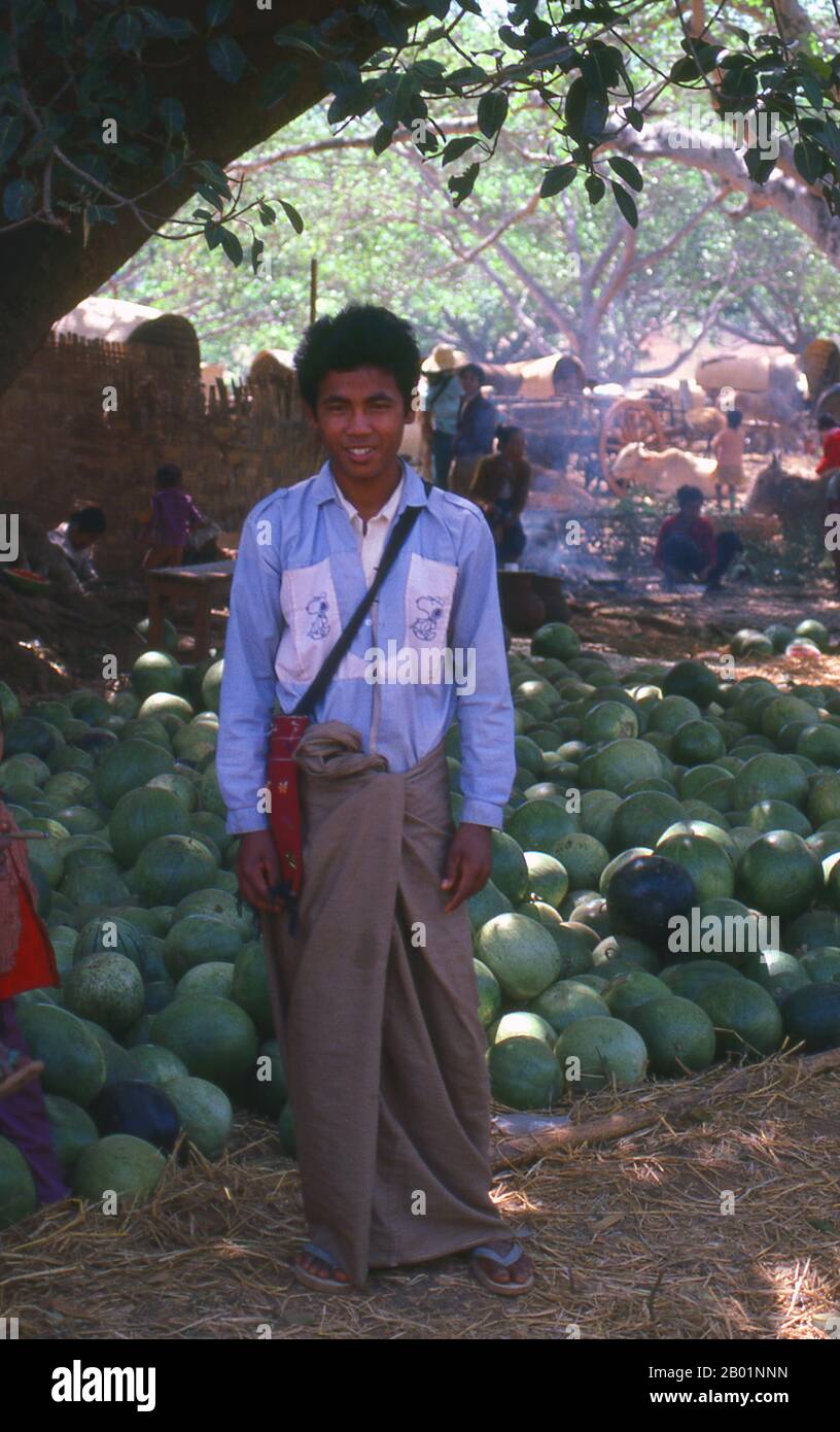 Burma/Myanmar: Watermelon seller near Pindaya, Shan State.  A longyi is a sheet of cloth widely worn in Burma. It is approximately 2 m (6½ ft.) long and 80 cm (2½ ft.) wide. The cloth is often sewn into a cylindrical shape. It is worn around the waist, running to the feet. It is held in place by folding fabric over, without a knot. It is also sometimes folded up to the knee for comfort. Similar garments are found in India, Bangladesh, Sri Lanka and the Malay Archipelago. In the Indian subcontinent (Bangladesh, West Bengal, South India, and Sri Lanka), it is known variously as a lungi or longi. Stock Photo