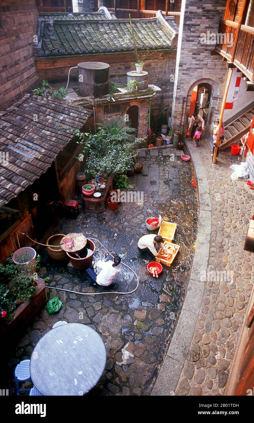 China: Family life in the inner courtyard at Zhenchang Lou Hakka Tower near Hukeng, Yongding County, Fujian Province.  The Hakka (Kejia in Mandarin; literally 'guest people') are Han Chinese who speak the Hakka language. Their distinctive earthen houses or tulou can be found in the borderland counties where Guangdong, Jiangxi and Fujian provinces meet.  Communal entities, tulou are fortified against marauding bandits and generally made of compacted earth, bamboo, wood and stone. They contain many rooms on several storeys, so that several families can live together. Stock Photo