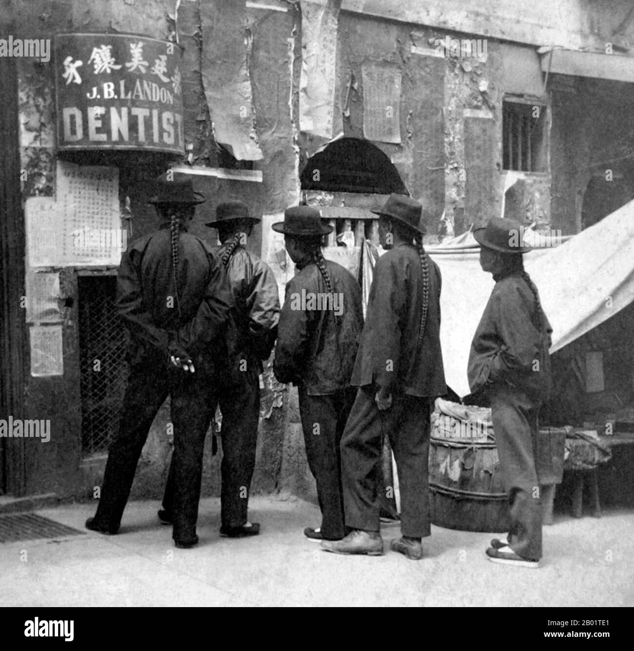 USA: Five Chinese men with queues reading a wall poster, San Francisco Chinatown, c. 1900.  San Francisco's Chinatown was the port of entry for early Hoisanese and Zhongshanese Chinese immigrants from the Guangdong province of southern China from the 1850s to the 1900s. The area was the one geographical region deeded by the city government and private property owners which allowed Chinese persons to inherit and inhabit dwellings within the city.  The majority of these Chinese shopkeepers, restaurant owners, and hired workers in San Francisco Chinatown were predominantly Hoisanese and male. Stock Photo