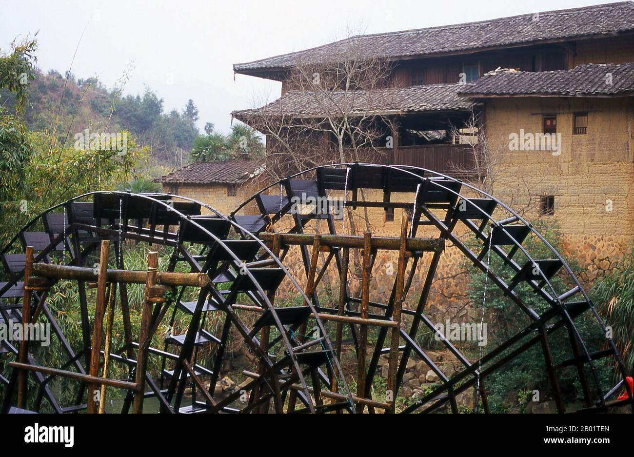 China: Waterwheels serving the Hakka earth houses near Hukeng, Yongding County, Fujian Province.  The Hakka (Kejia in Mandarin; literally 'guest people') are Han Chinese who speak the Hakka language. Their distinctive earthen houses or tulou can be found in the borderland counties where Guangdong, Jiangxi and Fujian provinces meet.  Communal entities, tulou are fortified against marauding bandits and generally made of compacted earth, bamboo, wood and stone. They contain many rooms on several storeys, so that several families can live together. Stock Photo