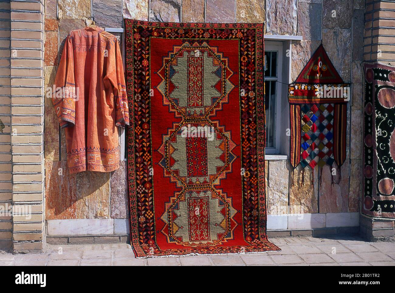 Uzbekistan: Carpet and clothing for sale in Samarkand.  Samarkand (Uzbek: Samarqand, from Sogdian: 'Stone Fort' or 'Rock Town') is the second-largest city in Uzbekistan and the capital of Samarqand Province. The city is most noted for its central position on the Silk Road between China and the West, and for being an Islamic centre for scholarly study.  In the 14th century it became the capital of the empire of Timur (Tamerlane) and is the site of his mausoleum (the Gur-e Amir). The Bibi-Khanym Mosque remains one of the city's most notable landmarks. Stock Photo