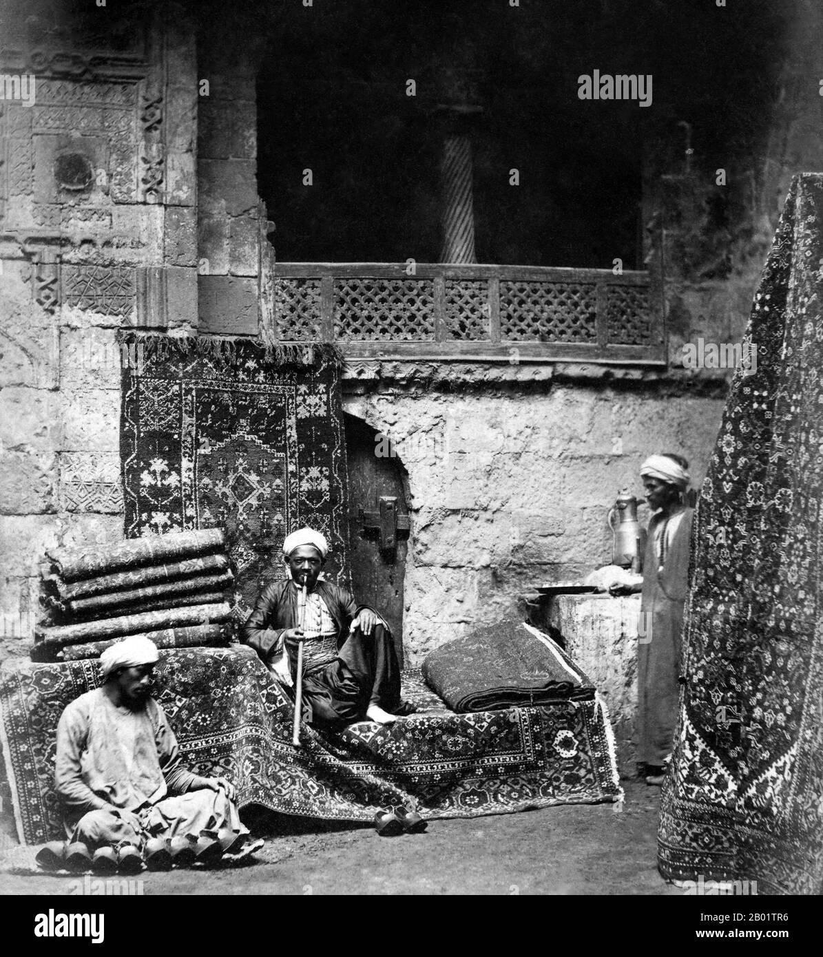 Egypt: Carpet sellers in Cairo. Photo by the Adelphoi Zangaki/Zangaki Brothers, late 19th century.  An authentic oriental rug is a handmade carpet that is either knotted with pile or woven without pile.  By definition - Oriental rugs are rugs that come from the orient. The simple definition of the term would be - rugs that come from (were made in) an Asian Country such as: China and Vietnam in the east to Turkey, Maghreb countries, Cyprus and Iran in the west and the Caucasus in the north to India in the south. Stock Photo