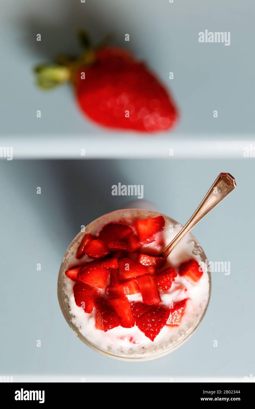 Natural yogurt with pieces of strawberries in a crystal glass on a blue background Stock Photo