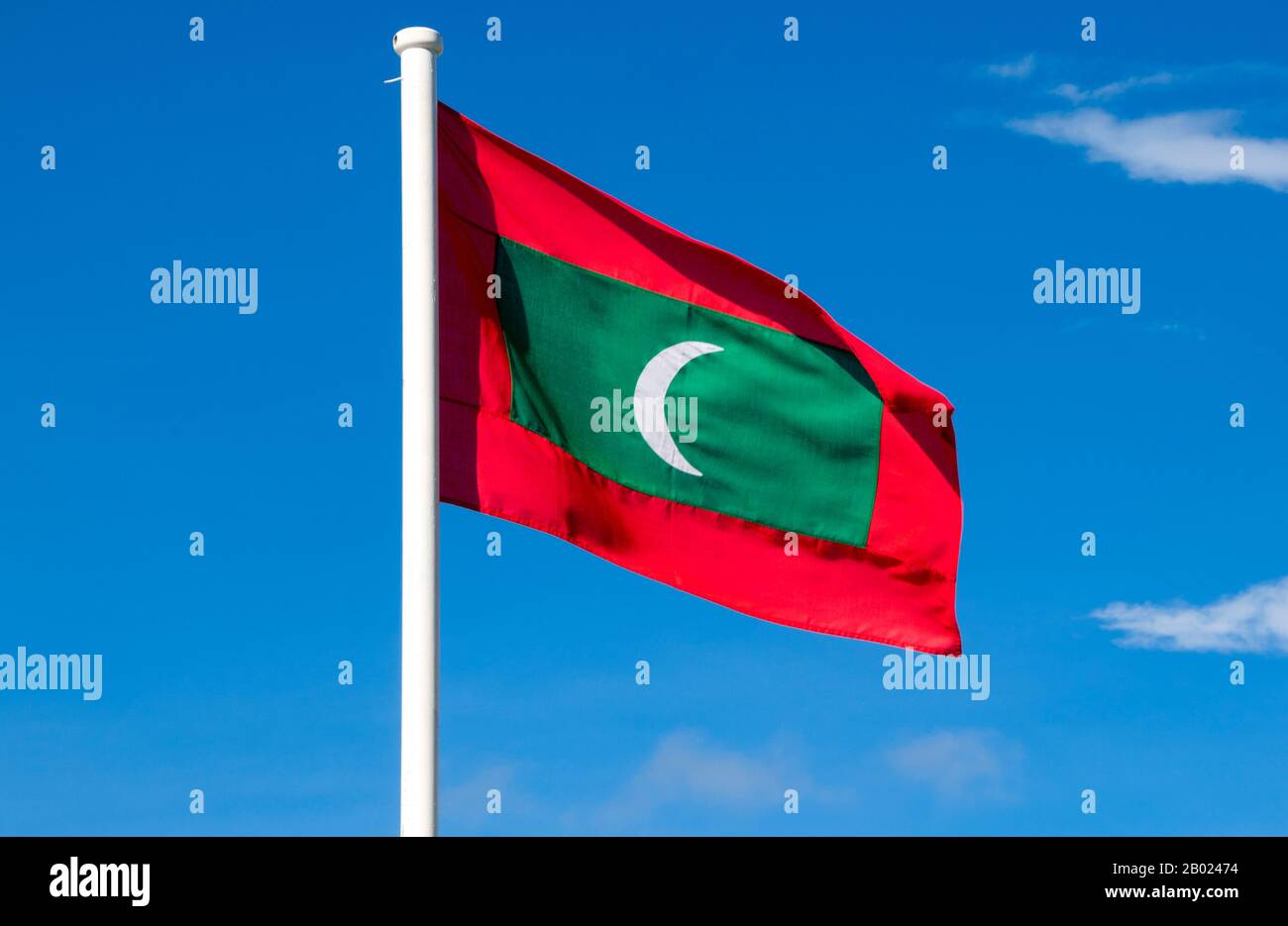 Maldives: Maldivian flag, Addu Atoll (Seenu Atoll). Asia's smallest and least-known nation, the Republic of Maldives, lies scattered from north to south across a 750-kilometre sweep of the Indian Ocean 500 kilometres south-west of Sri Lanka. More than 1000 islands, together with innumerable banks and reefs, are grouped in a chain of nineteen atolls which extends from a point due west of Colombo to just south of the equator.  The atolls, formed of great rings of coral based on the submarine Laccadive-Chagos ridge, vary greatly in size. Stock Photo