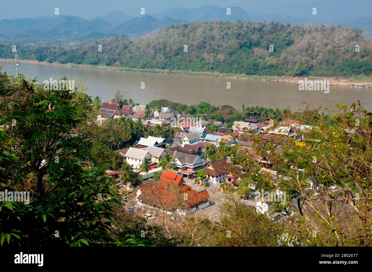 Laos: View from Phousi (Phu Si) Hill towards Wat Mai Suwannaphumaham and the Mekong River, Luang Prabang.  Wat Mai Suwannaphumaham dates from the early 19th century. The temple was once the residence of the Sangkhalat, the supreme patriarch of Buddhism in Laos.  The sim (ordination hall) is wooden, with a five-tiered roof in classic Luang Prabang style. The main attraction of the sim is the gilded walls of the front veranda, the designs of which recount scenes from the Ramayana and the Buddha’s penultimate incarnation (Vessantara Jataka). Stock Photo