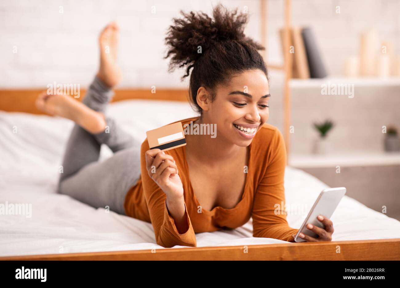 Girl Using Smartphone And Credit Card Lying In Bed Indoor Stock Photo