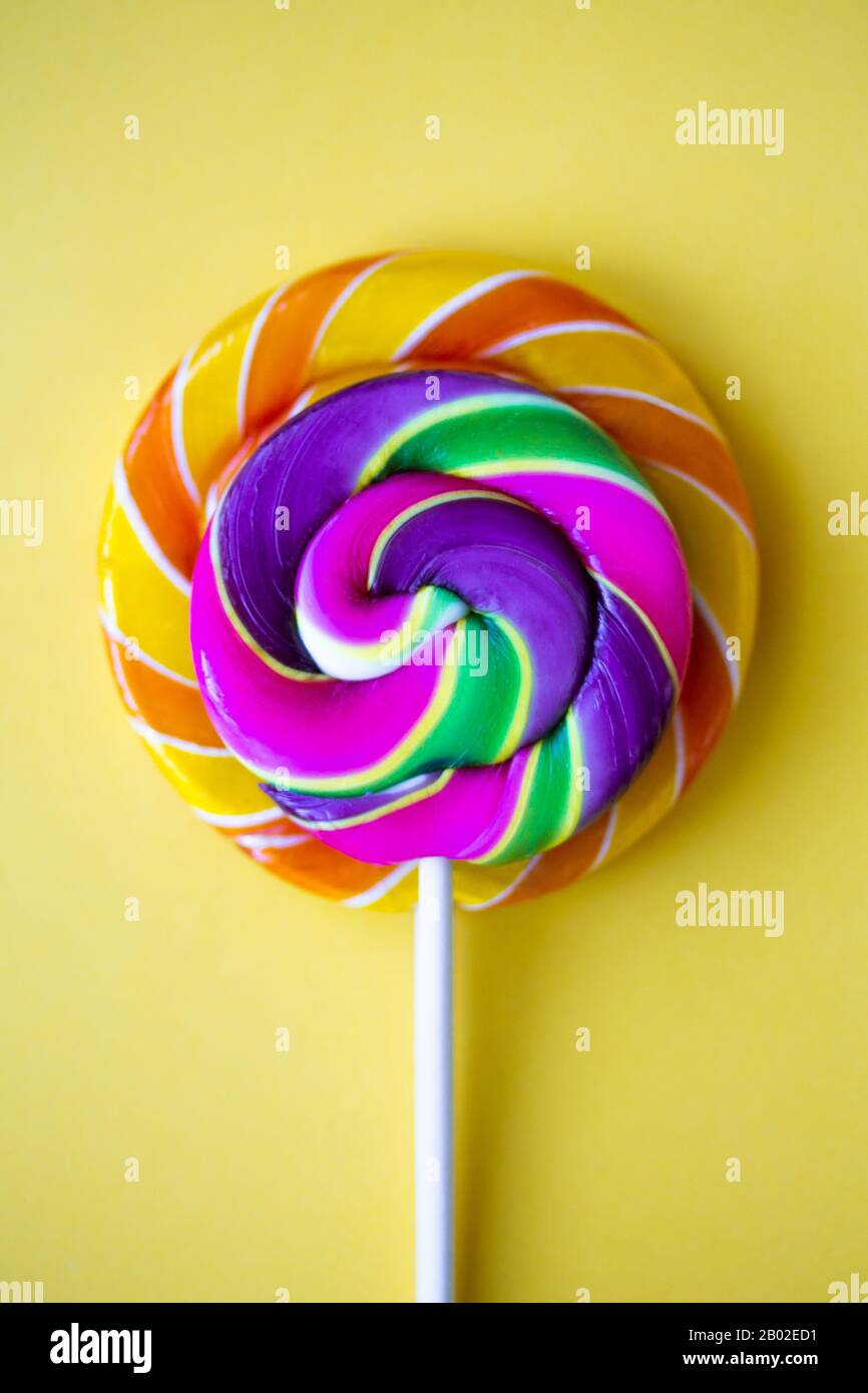 Bright swirl lollipops on yellow background. Festive vertical background with colorful twisted candies. Close up of rainbow round sweets on stick. Ora Stock Photo