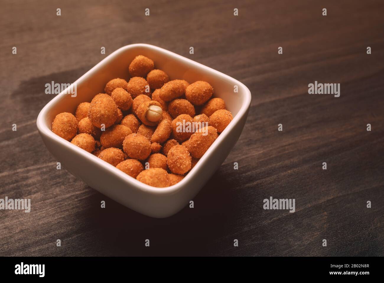 Salty peanut snack coated with barbecue sauce served in ceramic bowl on table Stock Photo