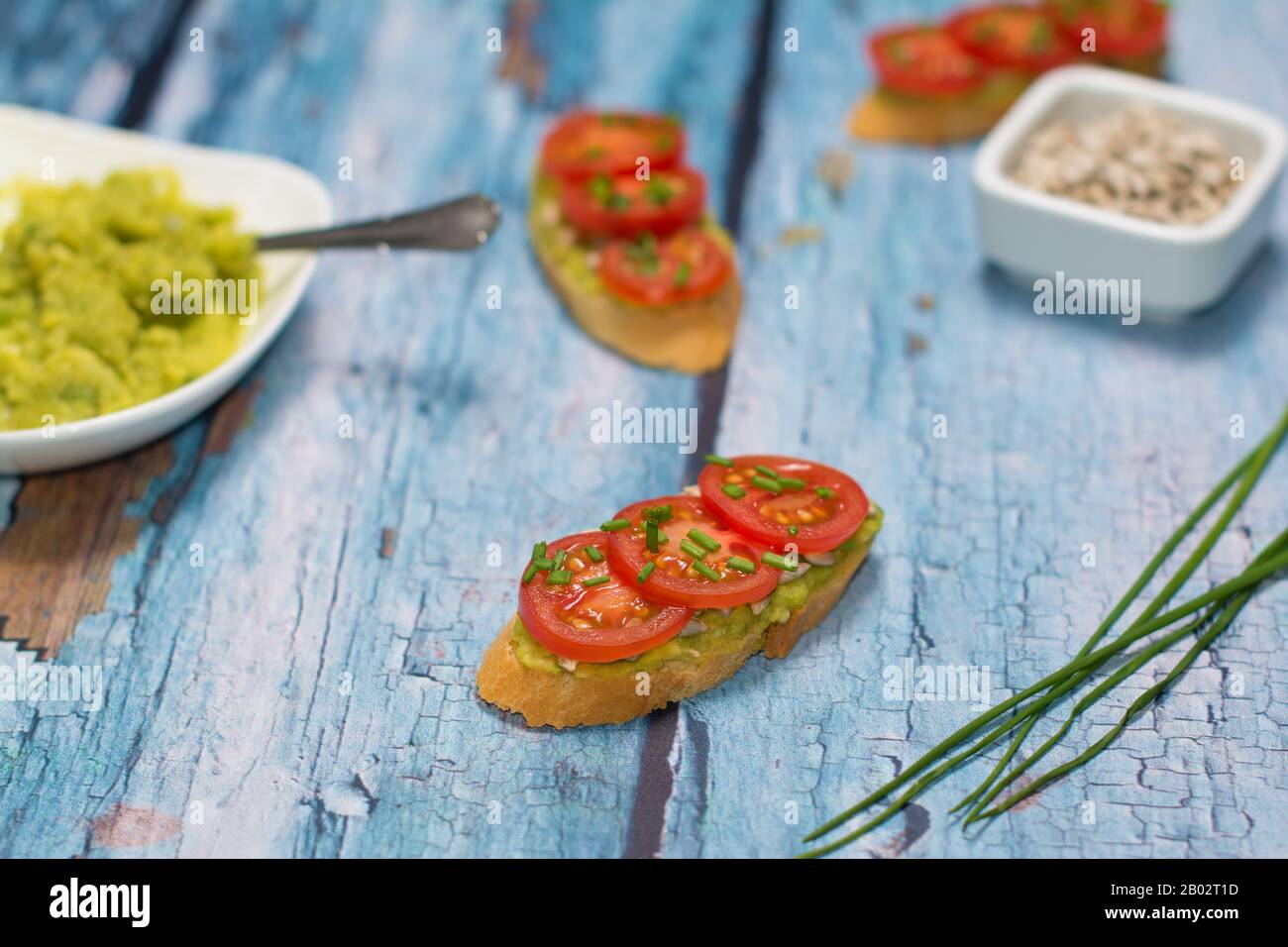 Open faced sandwiches. Open faced sandwich and a few chives green stalks beside it are lying in the foreground on a blue rustic background. Stock Photo