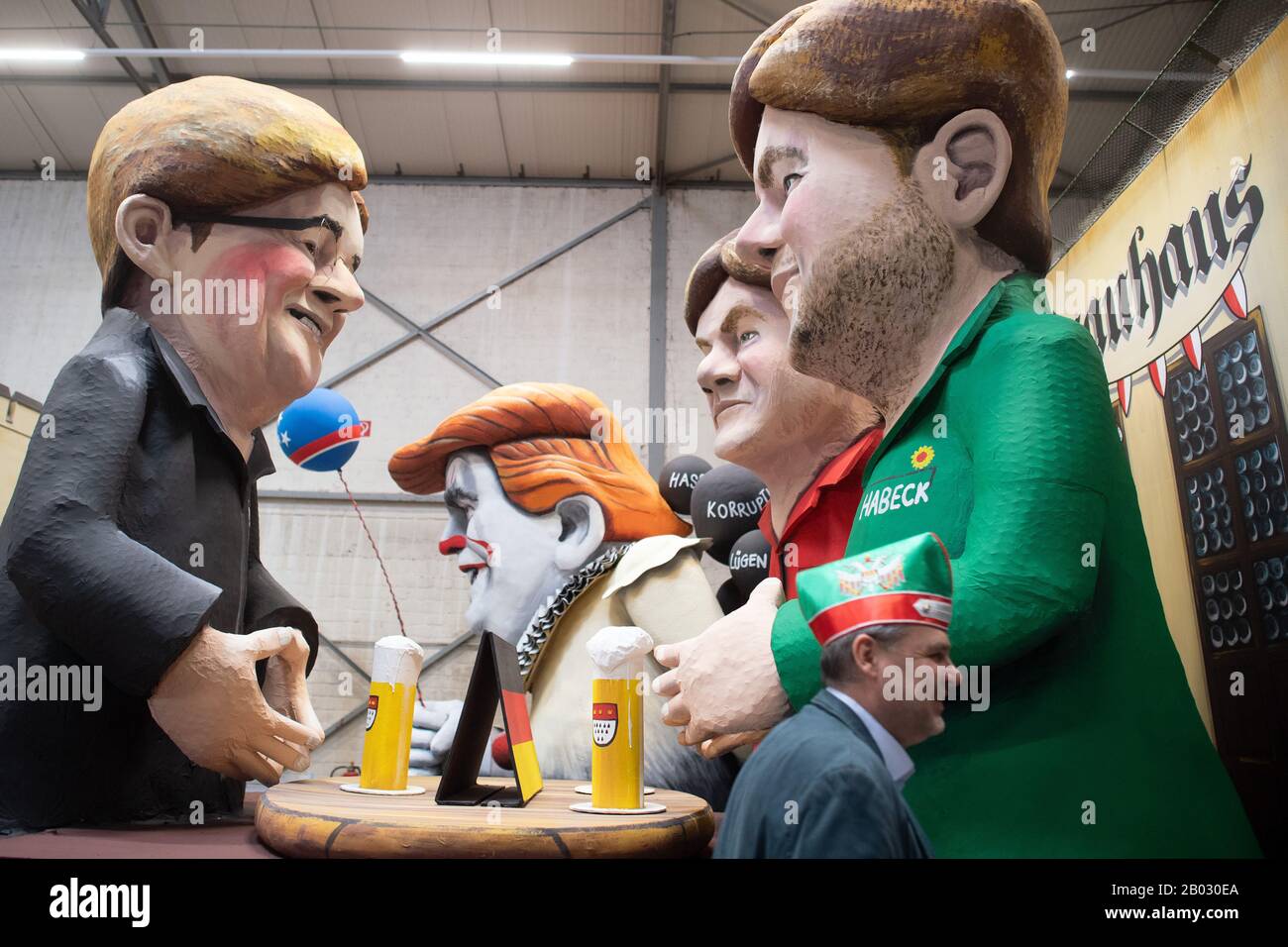 Cologne, Germany. 18th Feb, 2020. A visitor wearing a fool's cap walks past a carnival float with the cardboard figures of Armin Laschet (CDU, l), Robert Habeck (Bundnis90/Die Grünen, r) and Olav Scholz (SPD, M), who are negotiating for the chancellorship. The carriages of the Cologne Rose Monday Train were presented during the topping-out ceremony. Credit: Federico Gambarini/dpa/Alamy Live News Stock Photo