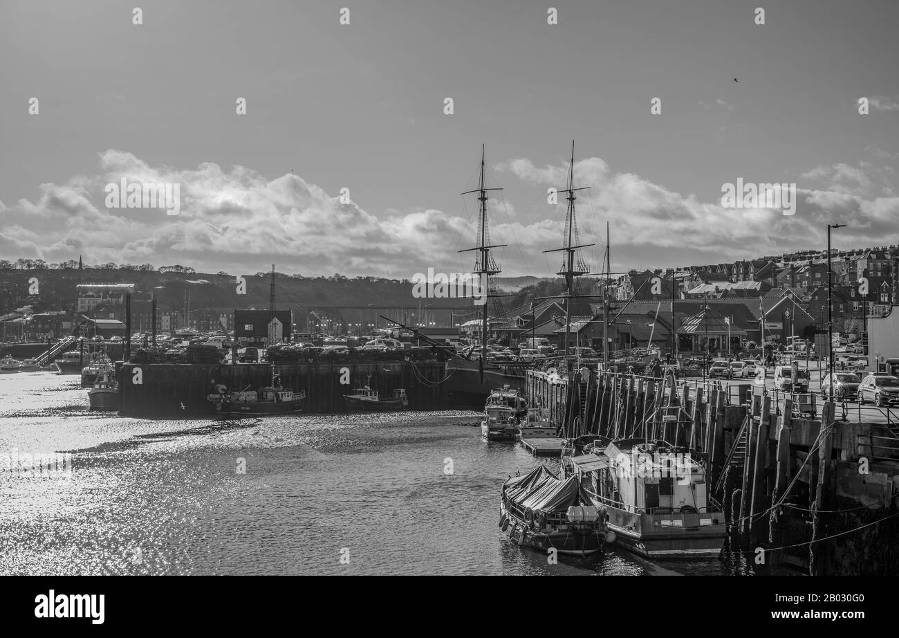 The inner harbour at Whitby.  Boats are moored to the wharf and the masts of the replica of HMS endeavour are silhouetted against the sky. Stock Photo